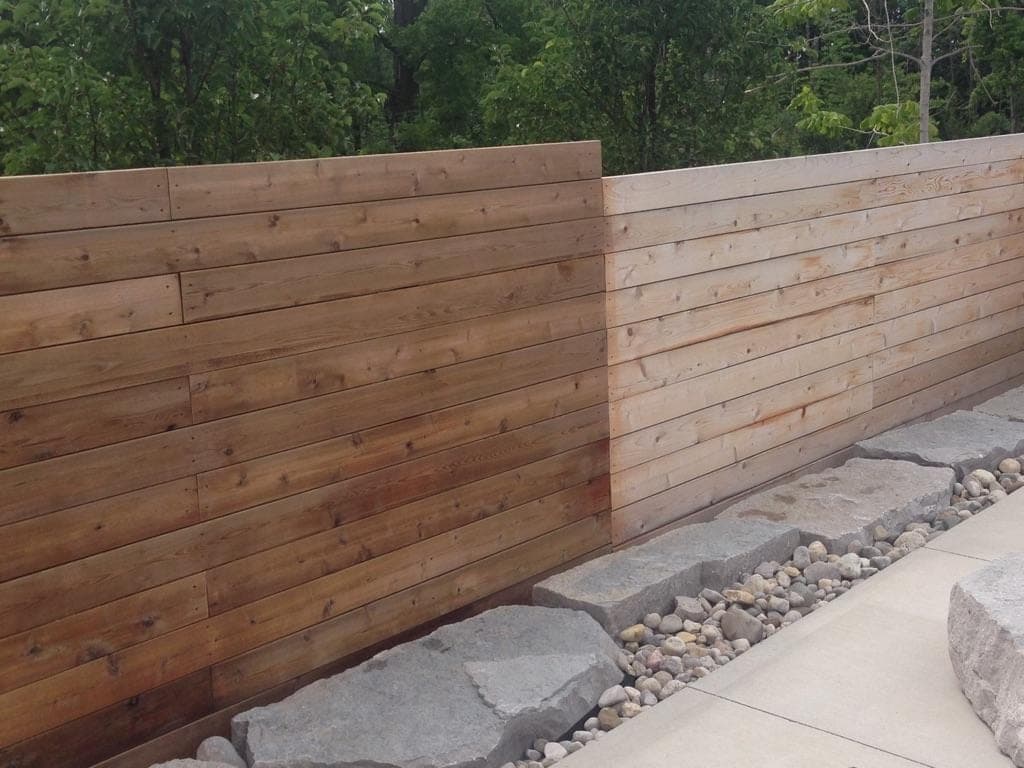 Finished cedar plank retaining wall with concrete cap and armour stone base along a patio