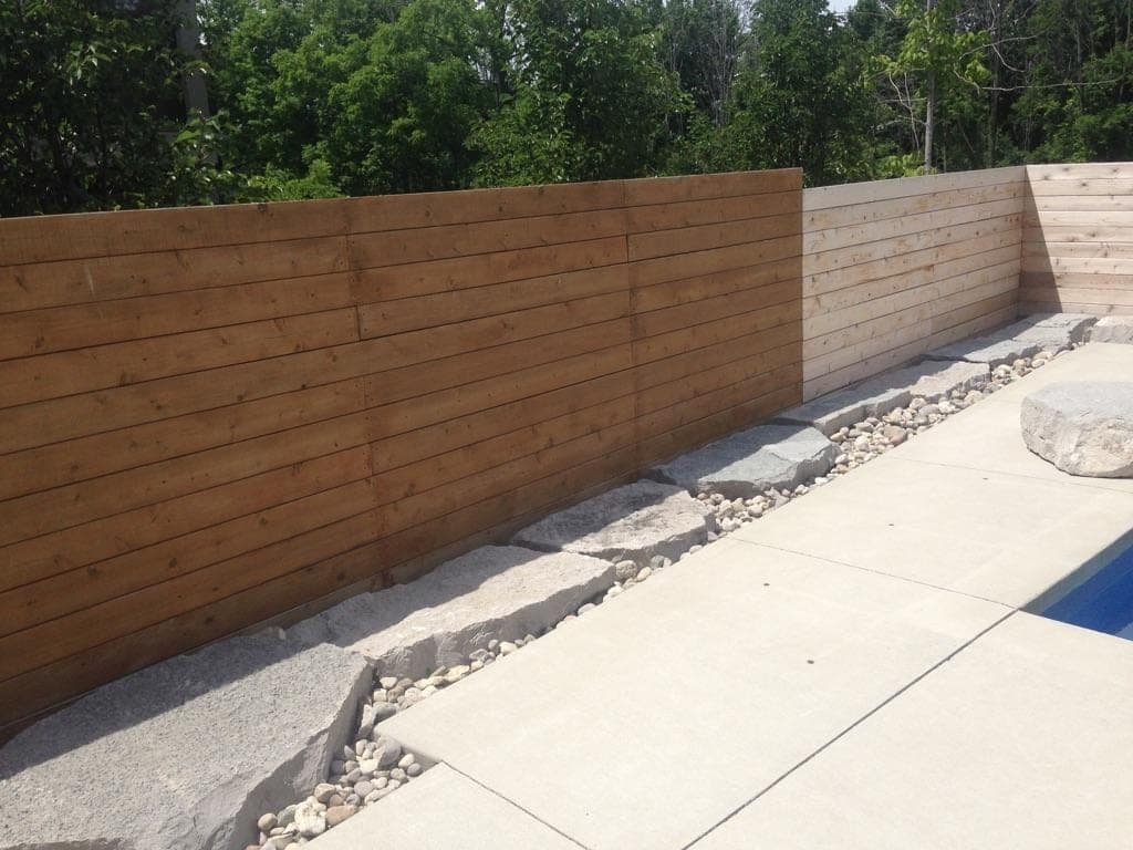 Horizontal cedar plank retaining wall with concrete cap bordering a poolside patio
