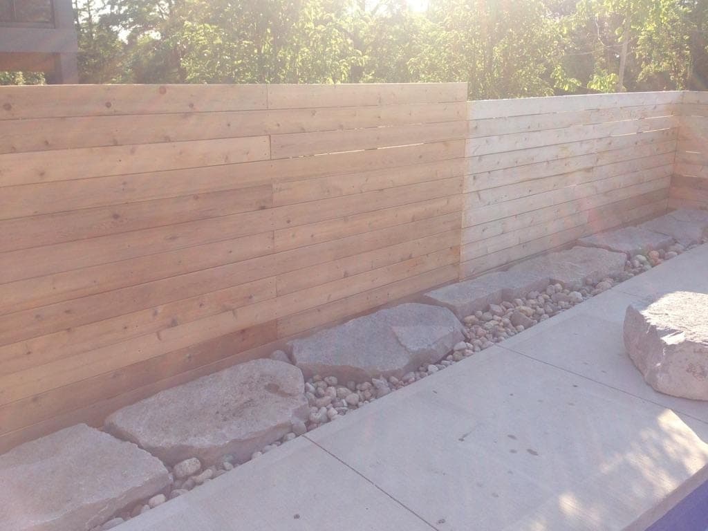 Horizontal cedar plank retaining wall with concrete cap and river rock boulder base
