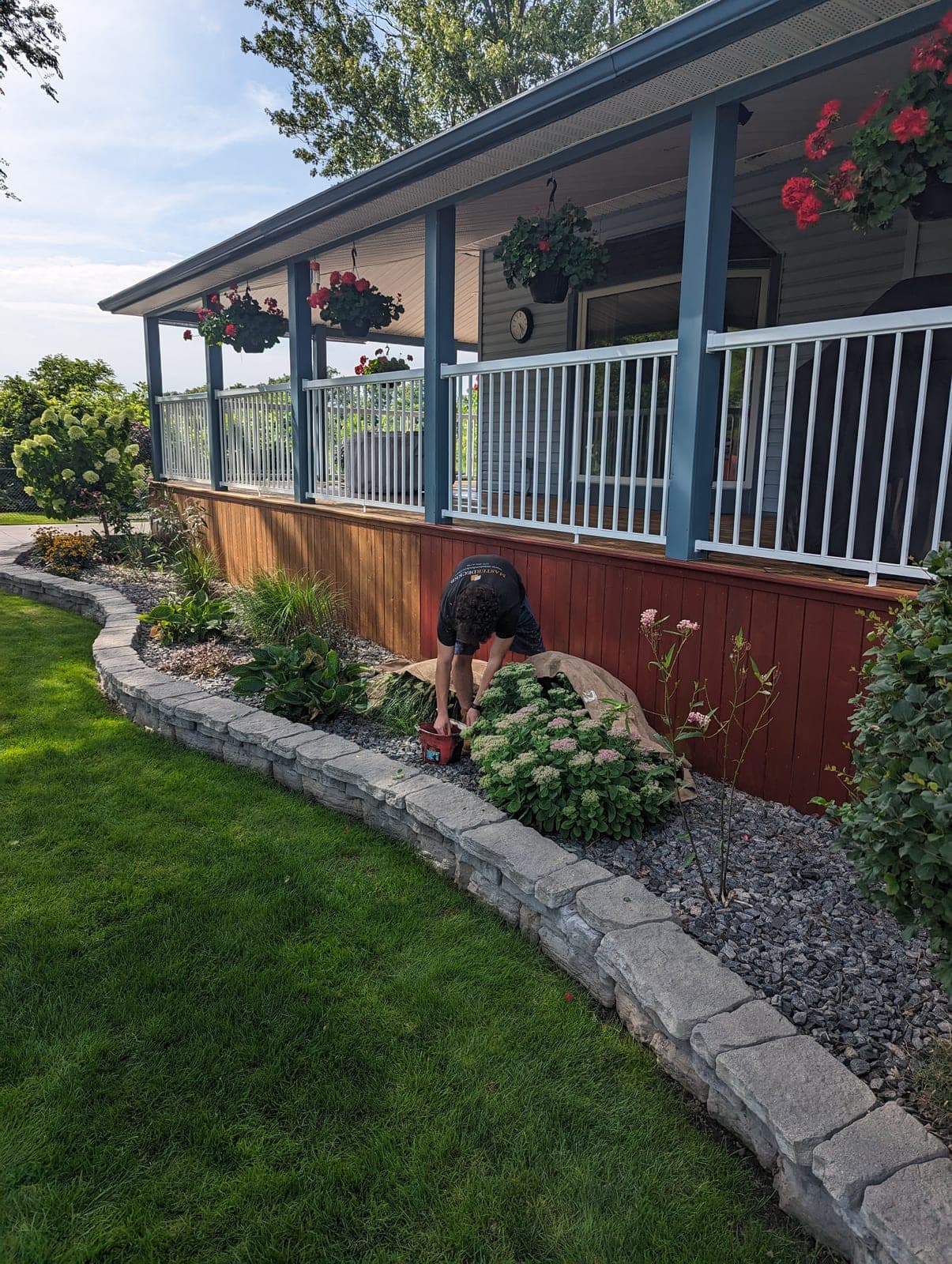 Curved stacked-block garden retaining wall holding a raised planting bed along a covered farmhouse porch