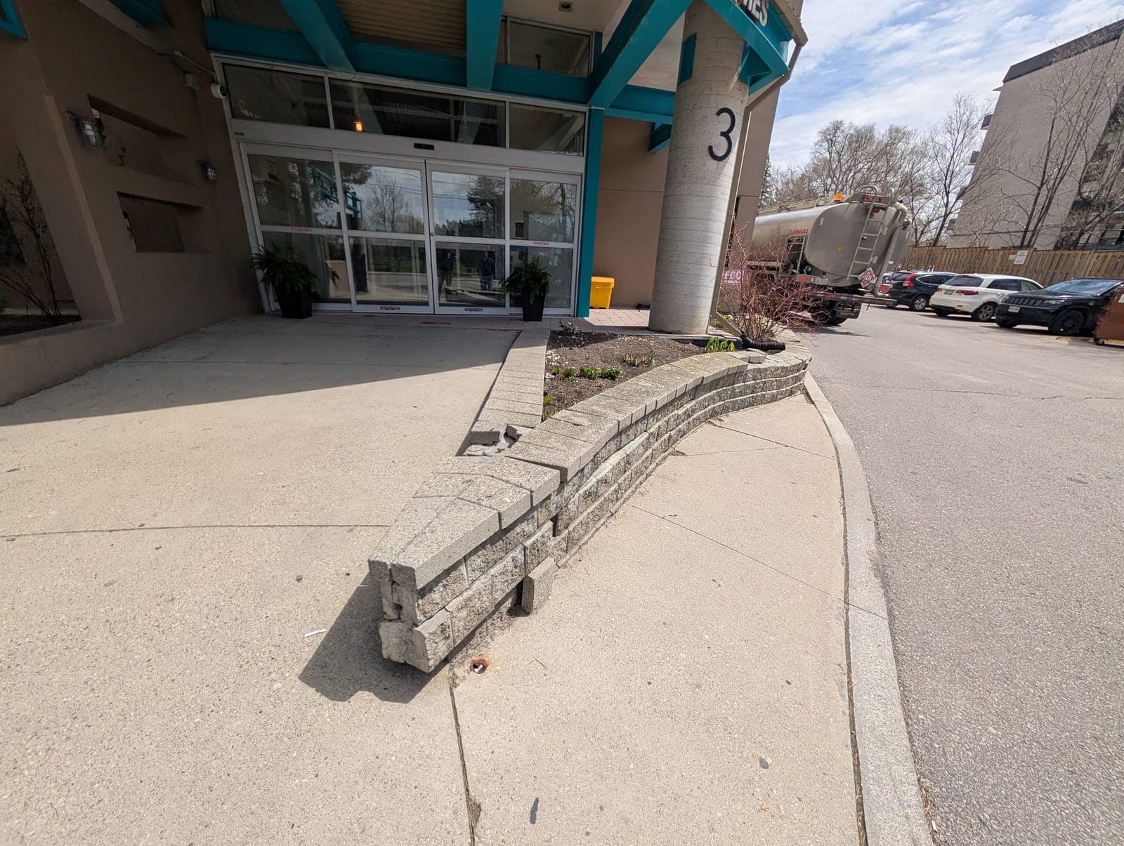 Damaged segmental block retaining wall with dislodged capstones along a commercial driveway