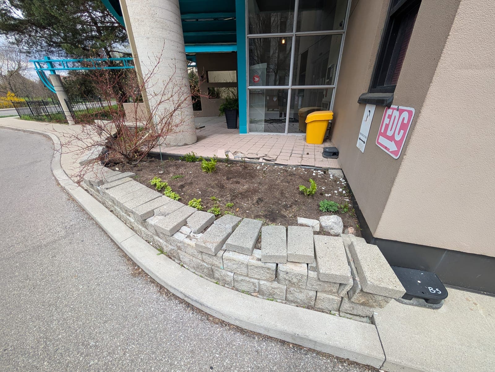 Segmental block retaining wall with dislodged blocks bordering a commercial planter bed
