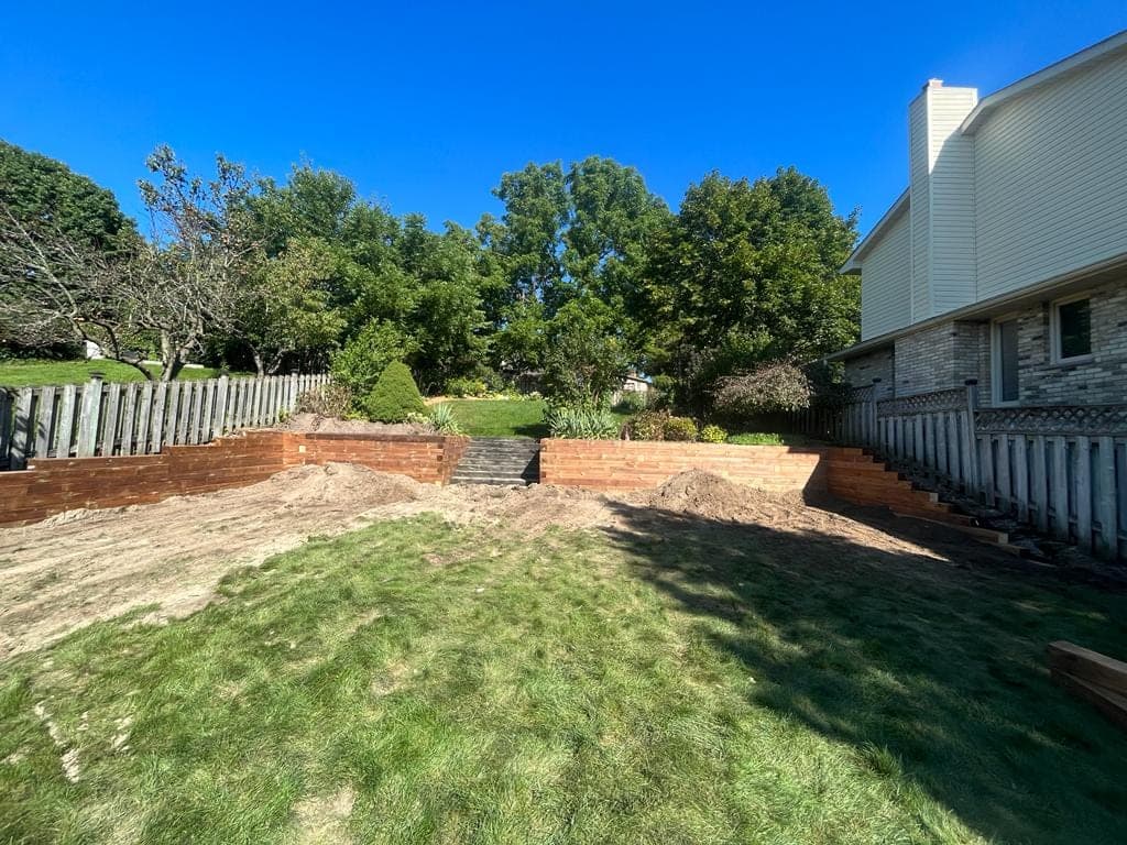 Two-section timber retaining wall with central steps separating a raised garden from the lawn