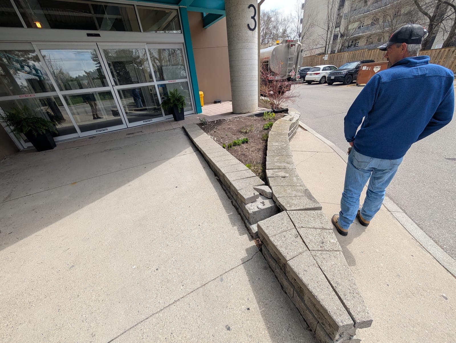 Contractor inspecting a failing segmental block retaining wall at a commercial property