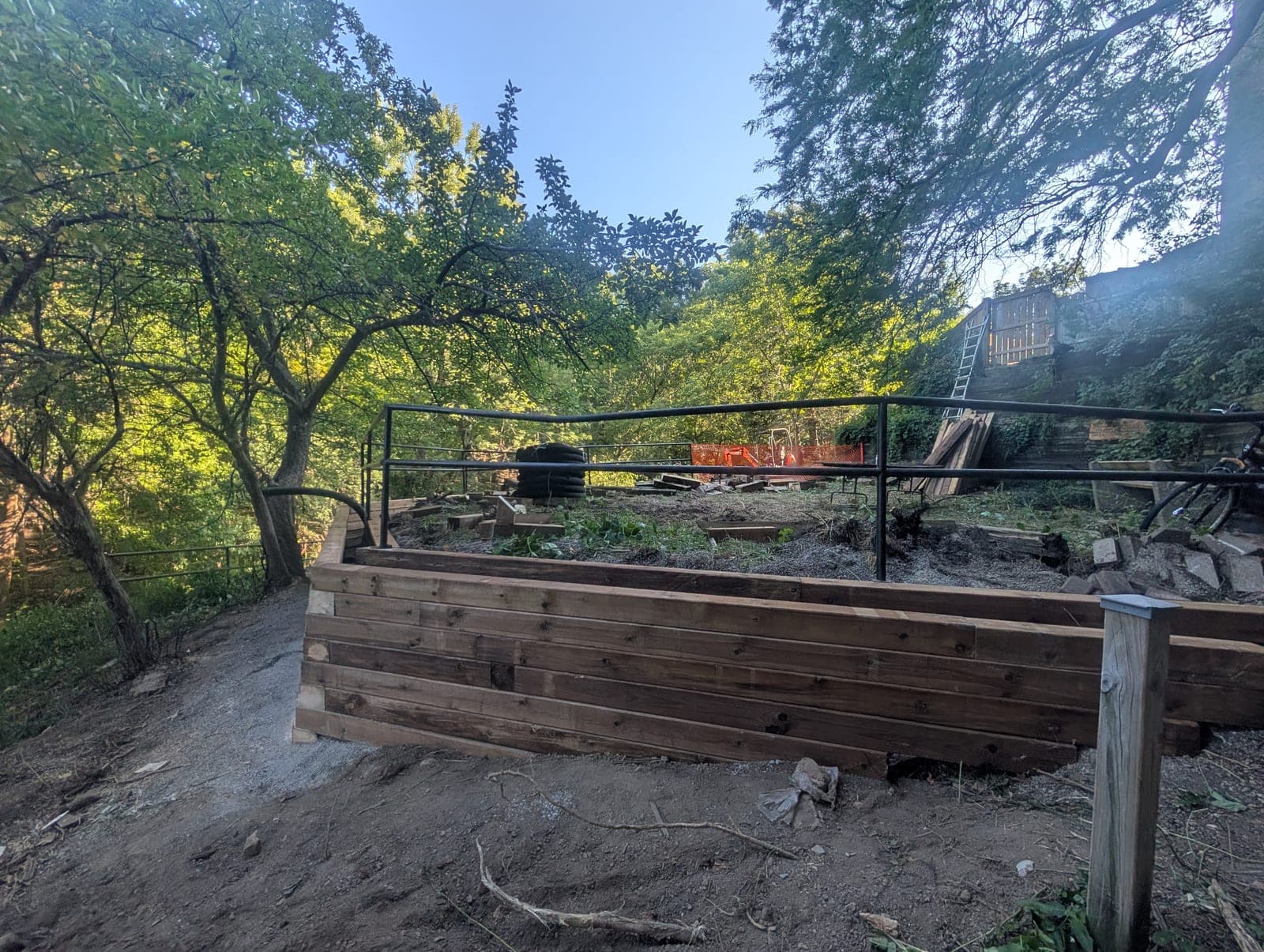 Finished timber retaining wall with black metal railing holding back a landscaped grade