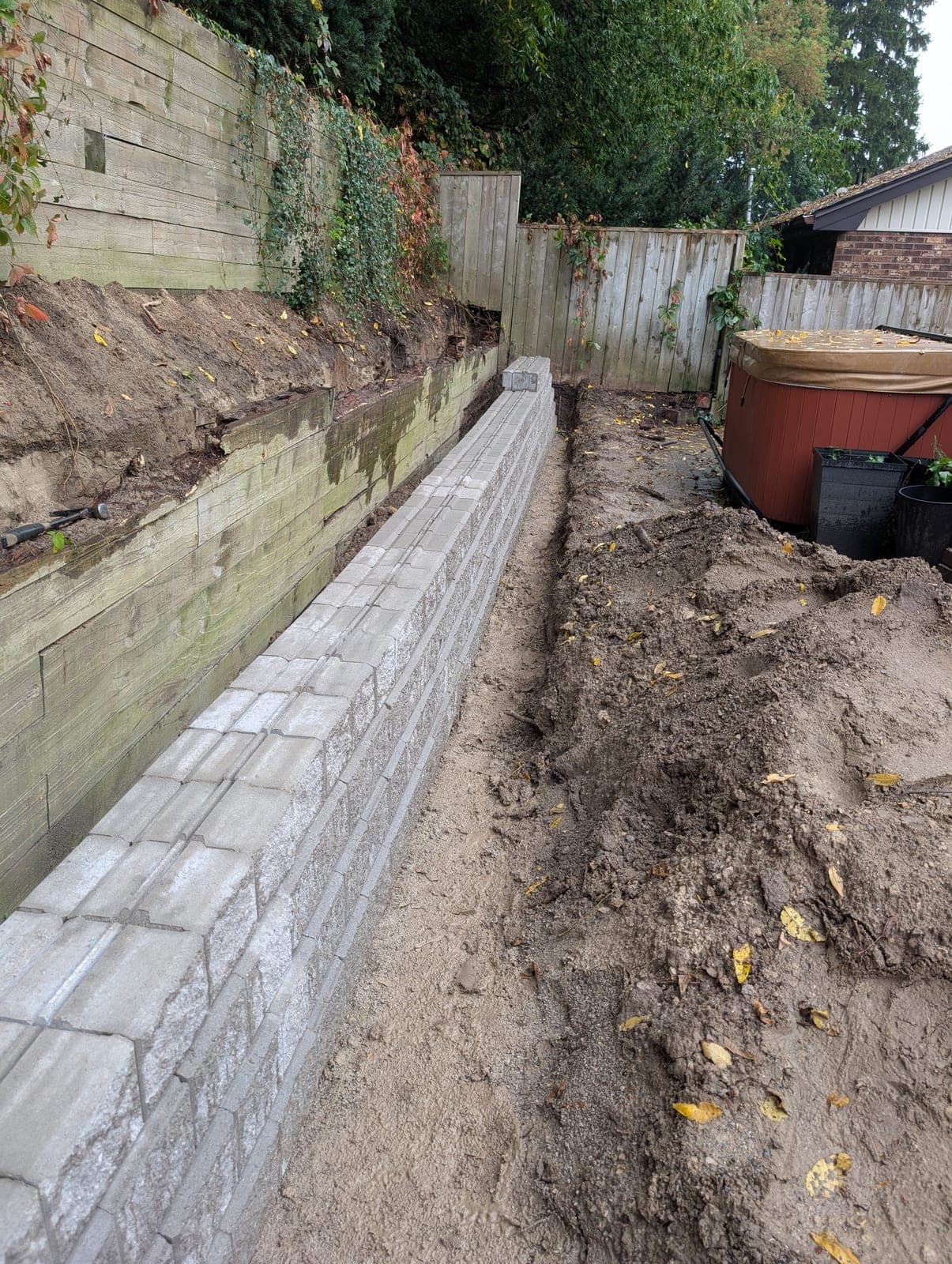 New segmental concrete block retaining wall installed at the base of a tall timber retaining wall