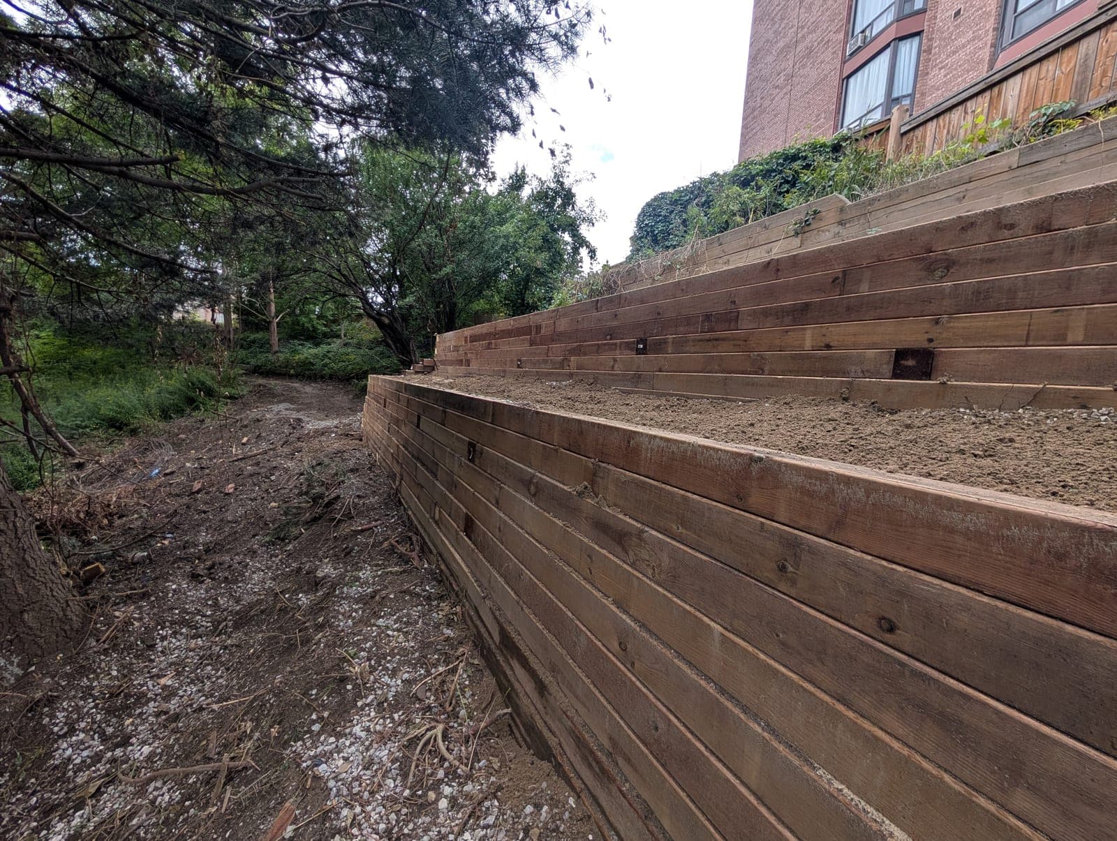 Long terraced timber retaining wall viewed along its length on a graded urban backyard slope