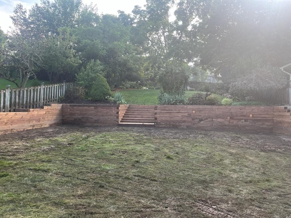 Long wood timber retaining wall with central access steps in a terraced London, Ontario backyard
