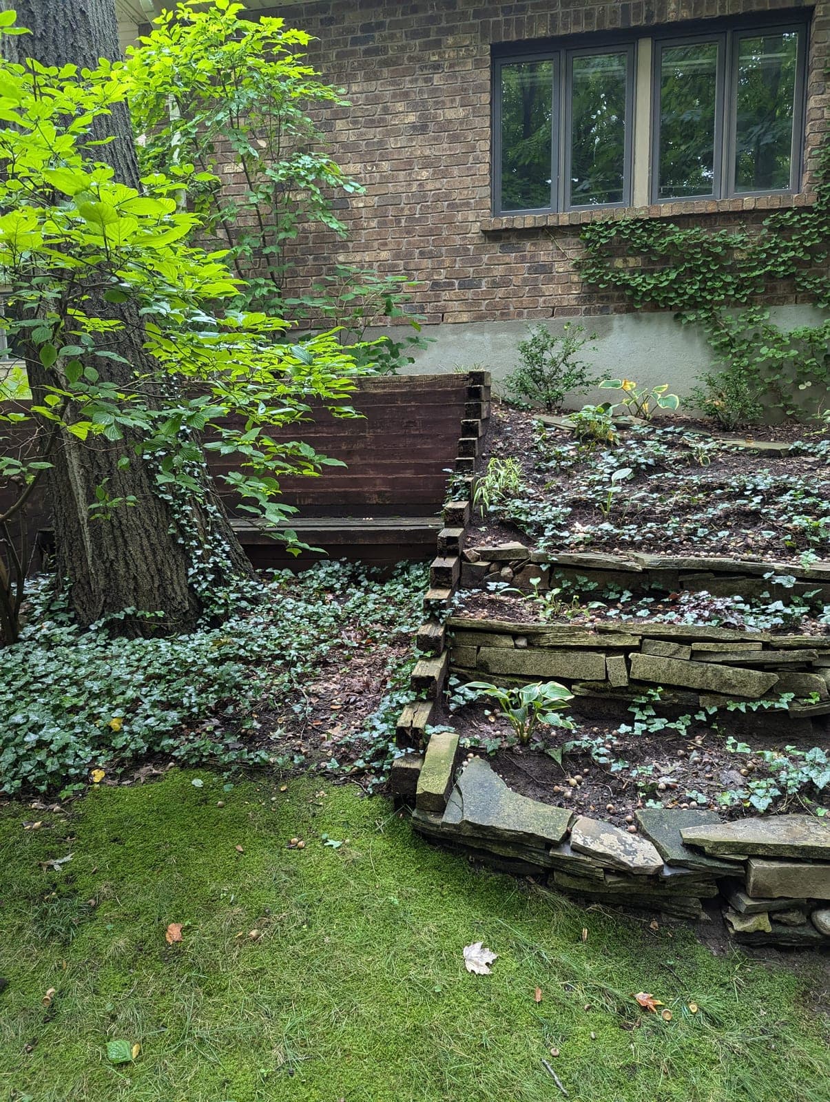 Natural stone retaining wall forming a terraced raised garden bed beside a brick home