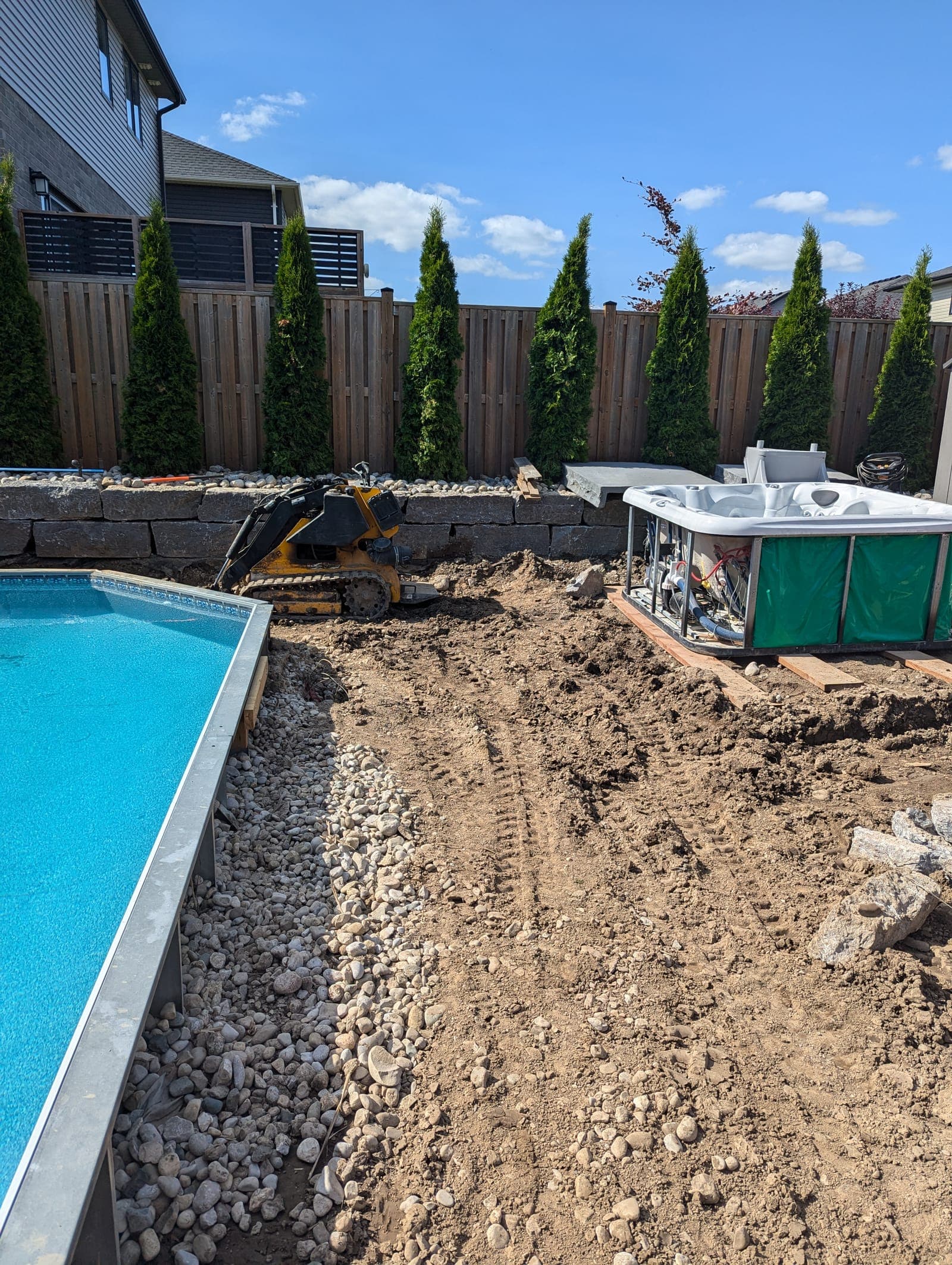 Low natural stone retaining wall running along the rear of a landscaped backyard pool