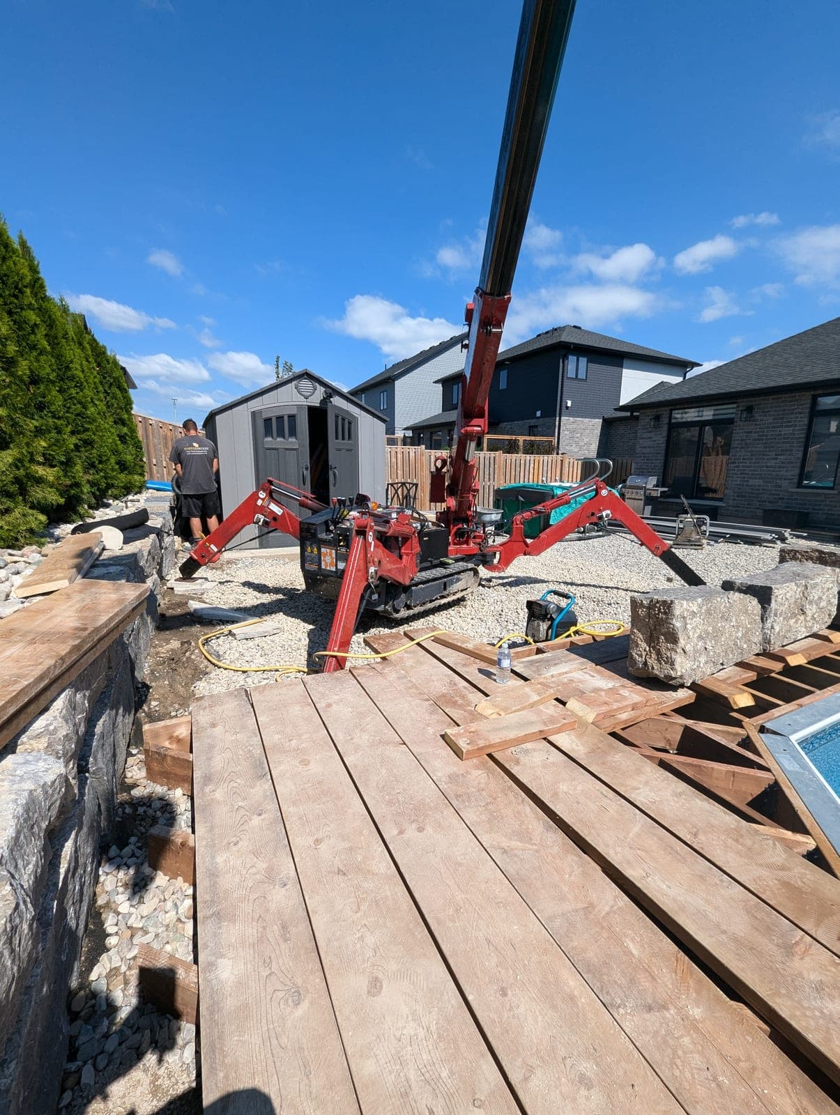 Natural stone retaining wall capped with timber beside a river-rock drainage bed in a backyard
