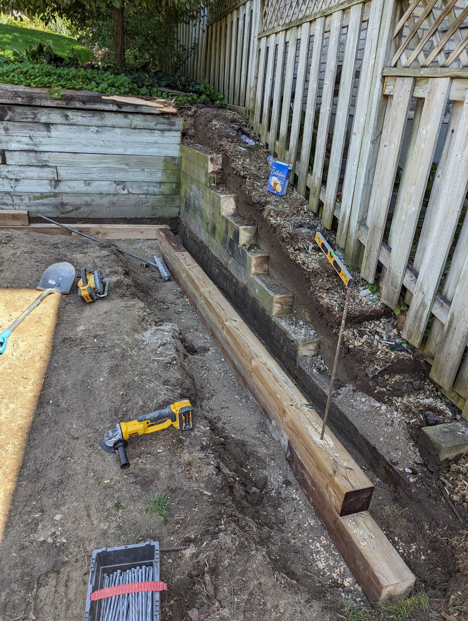 New pressure-treated timber retaining wall base course being installed beside an older timber wall