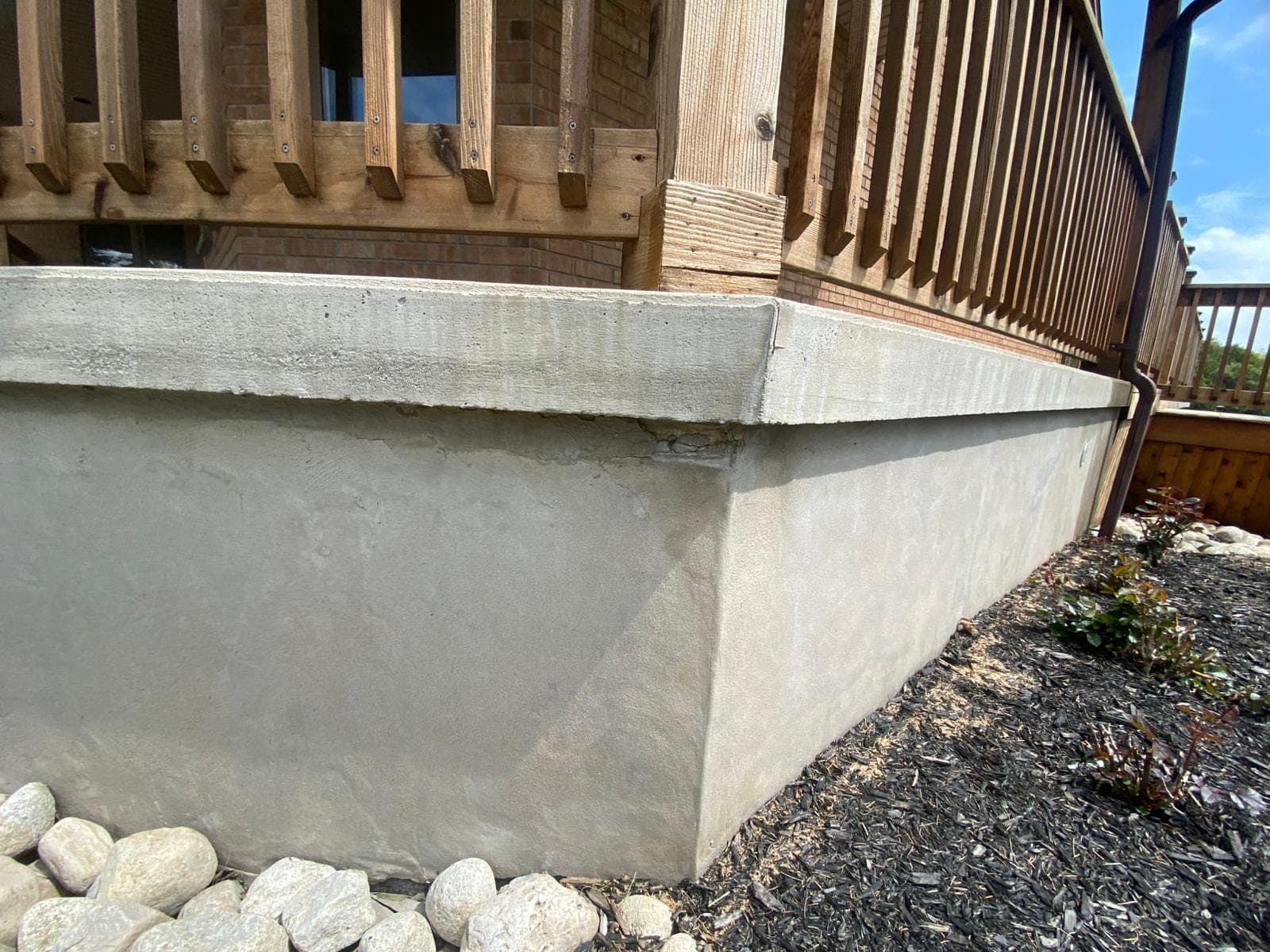 Parged poured concrete retaining wall bordering a mulched garden bed beside a raised backyard deck
