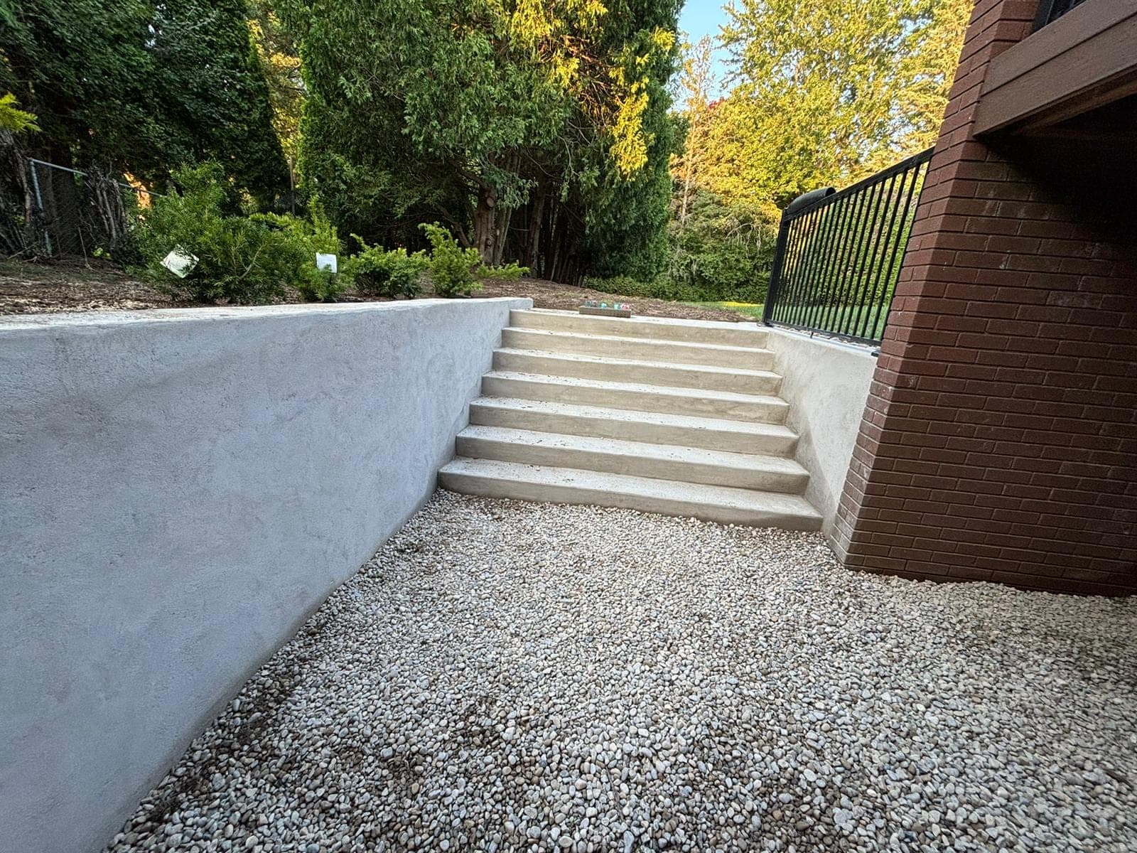 Finished parged poured concrete retaining wall flanking a concrete staircase beside a brick home