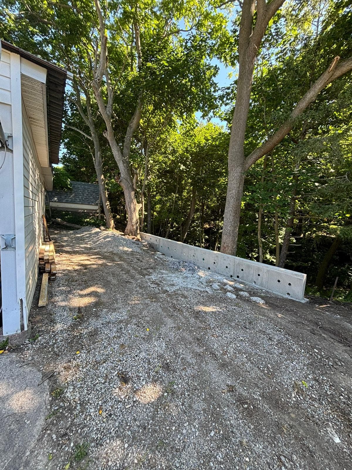 New poured concrete retaining wall holding back a treed hillside along a gravel pathway