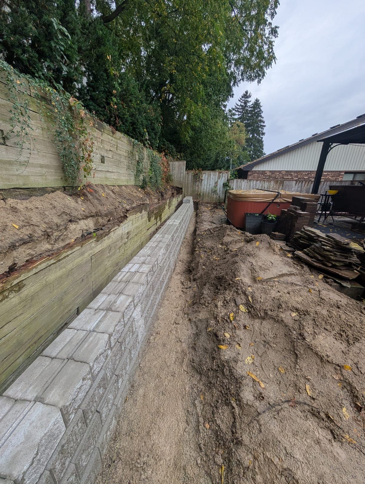 New segmental block retaining wall running along a backyard beneath a tall timber retaining wall