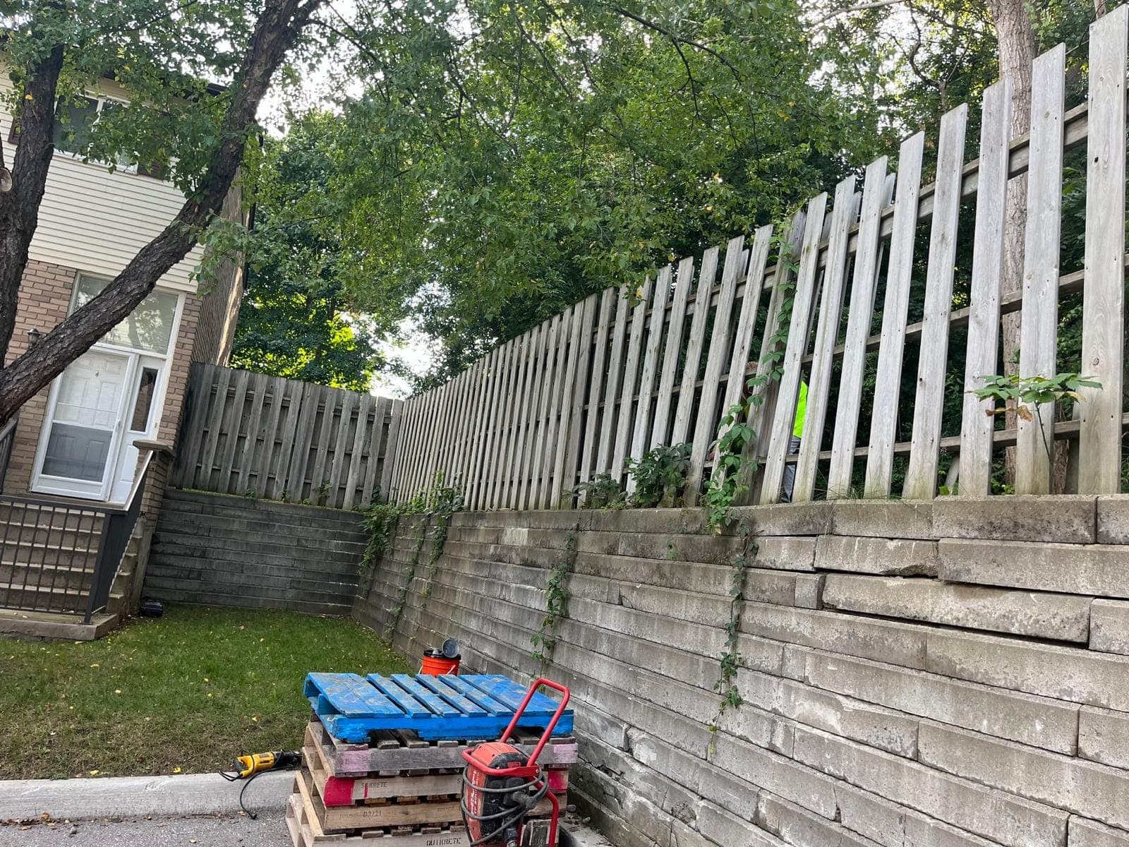 Weathered segmental concrete block retaining wall topped with a wood privacy fence along a driveway