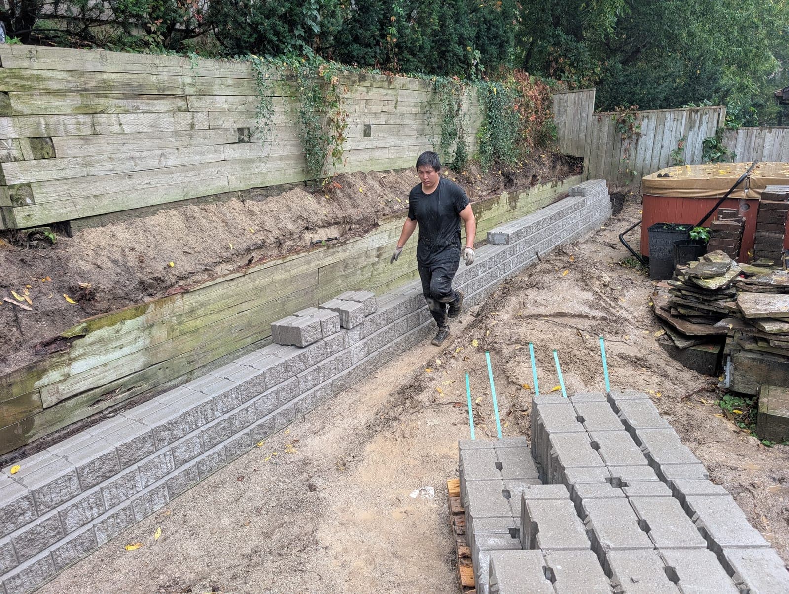 Long segmental concrete block retaining wall built beneath a tall tiered timber retaining wall