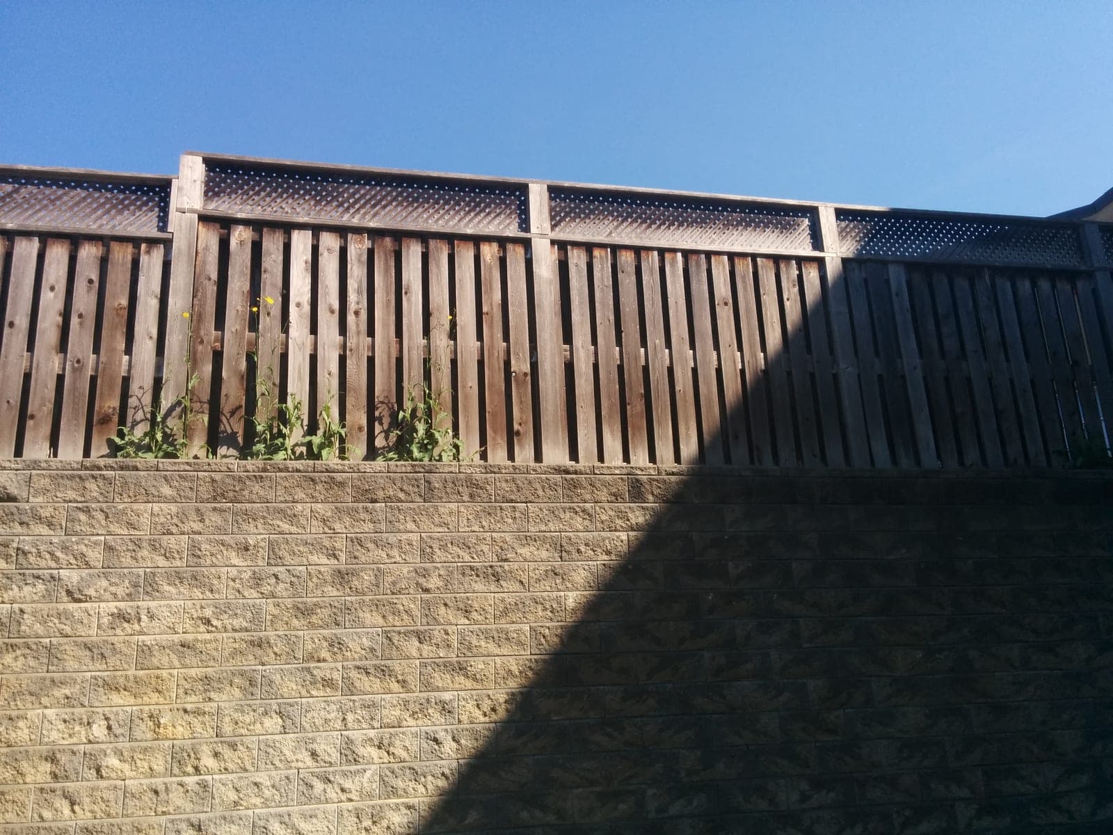 Segmental block retaining wall with a wooden fence on top under a clear blue sky