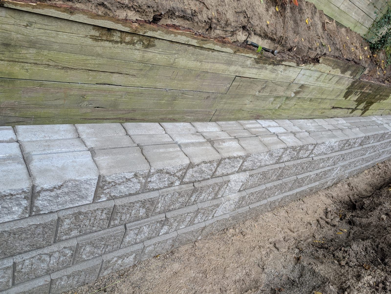 Close-up of a segmental concrete block retaining wall with capstones below a timber retaining wall