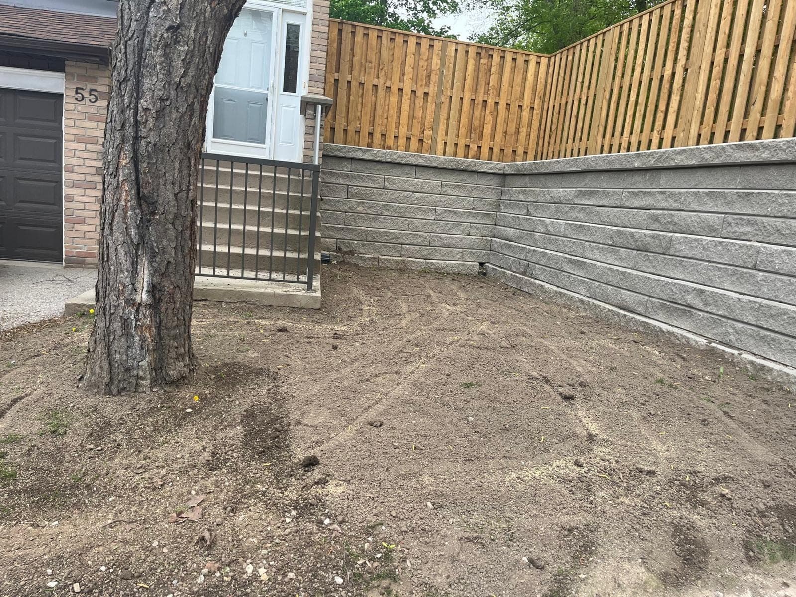 New grey segmental block retaining wall with a corner return beneath a cedar fence