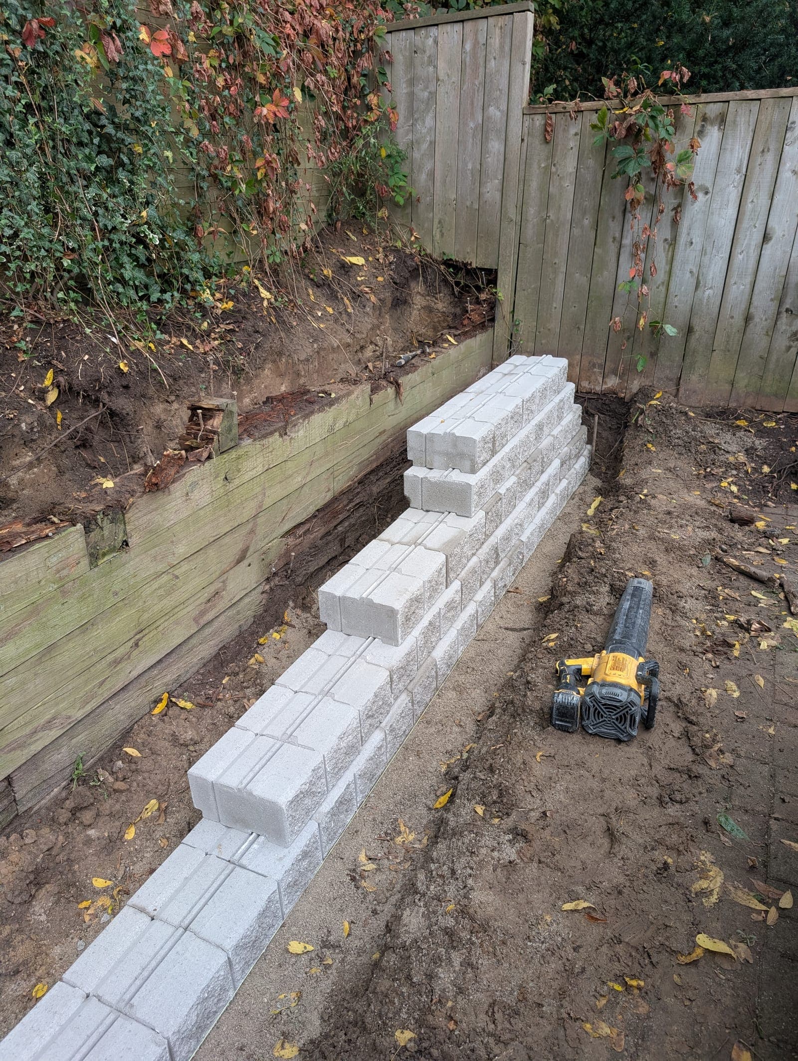 Segmental concrete block retaining wall under construction below an old timber retaining wall