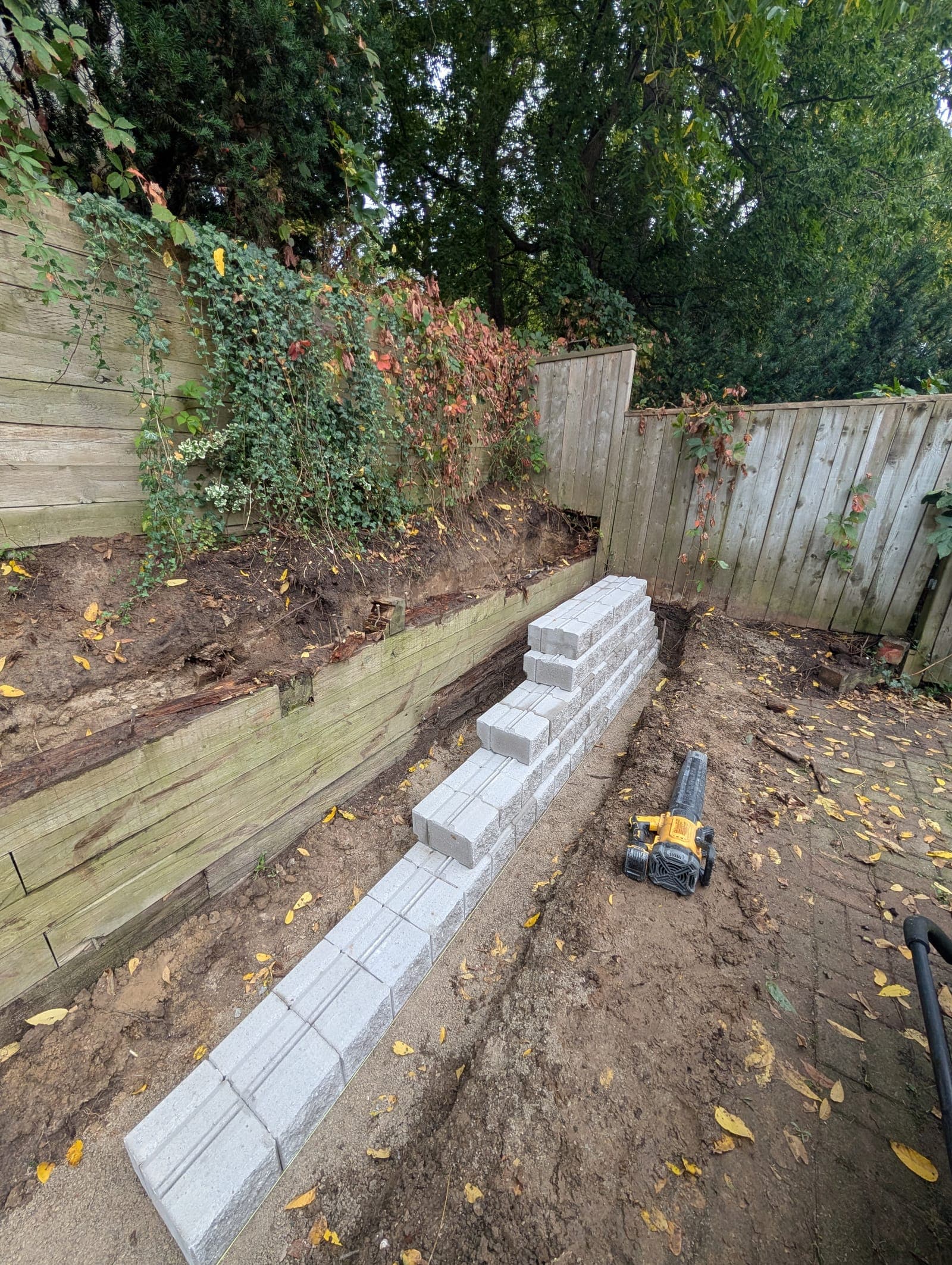 New segmental concrete block retaining wall being started in front of an existing timber retaining wall