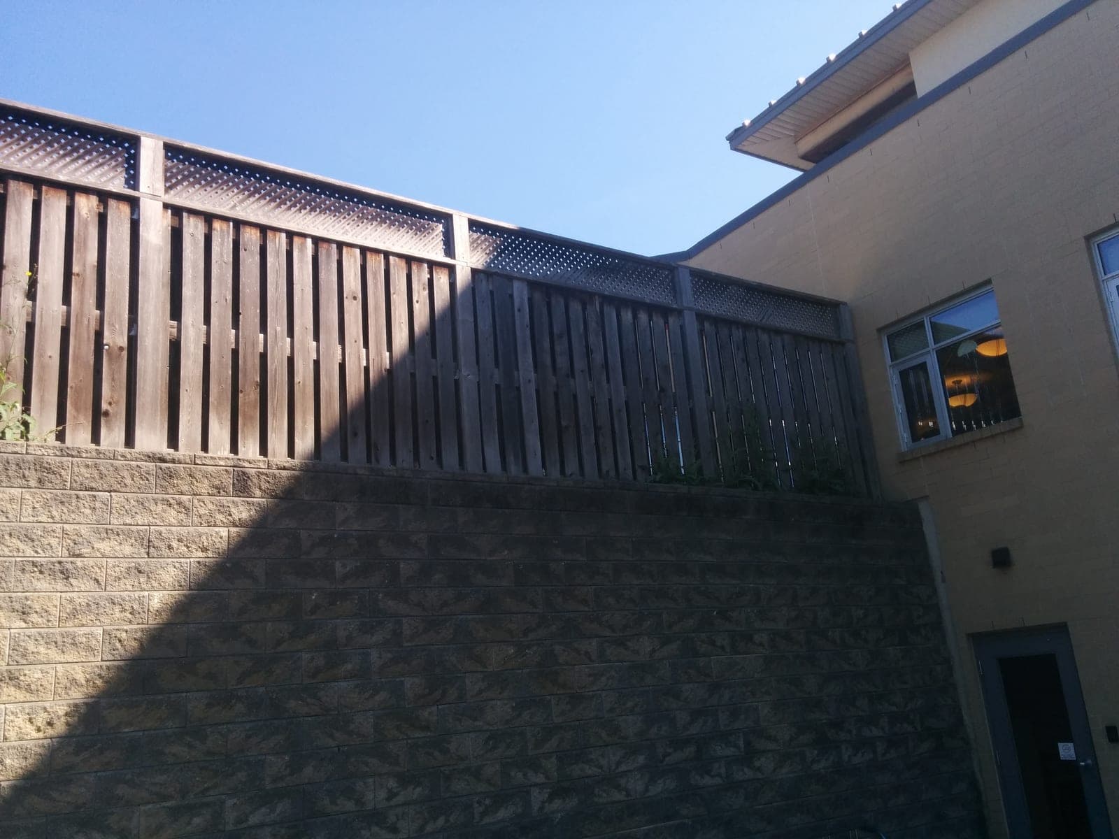 Tall segmental block retaining wall topped with a wooden privacy fence beside a building