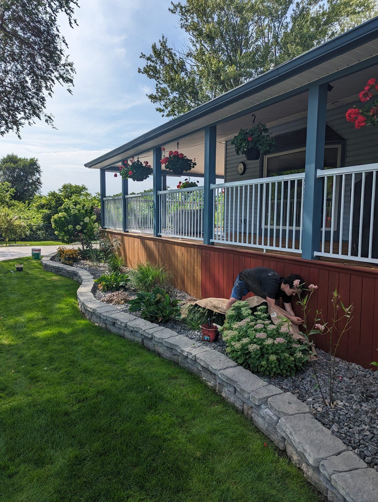 Low curved stacked-block retaining wall creating a raised garden bed beside a country porch and green lawn