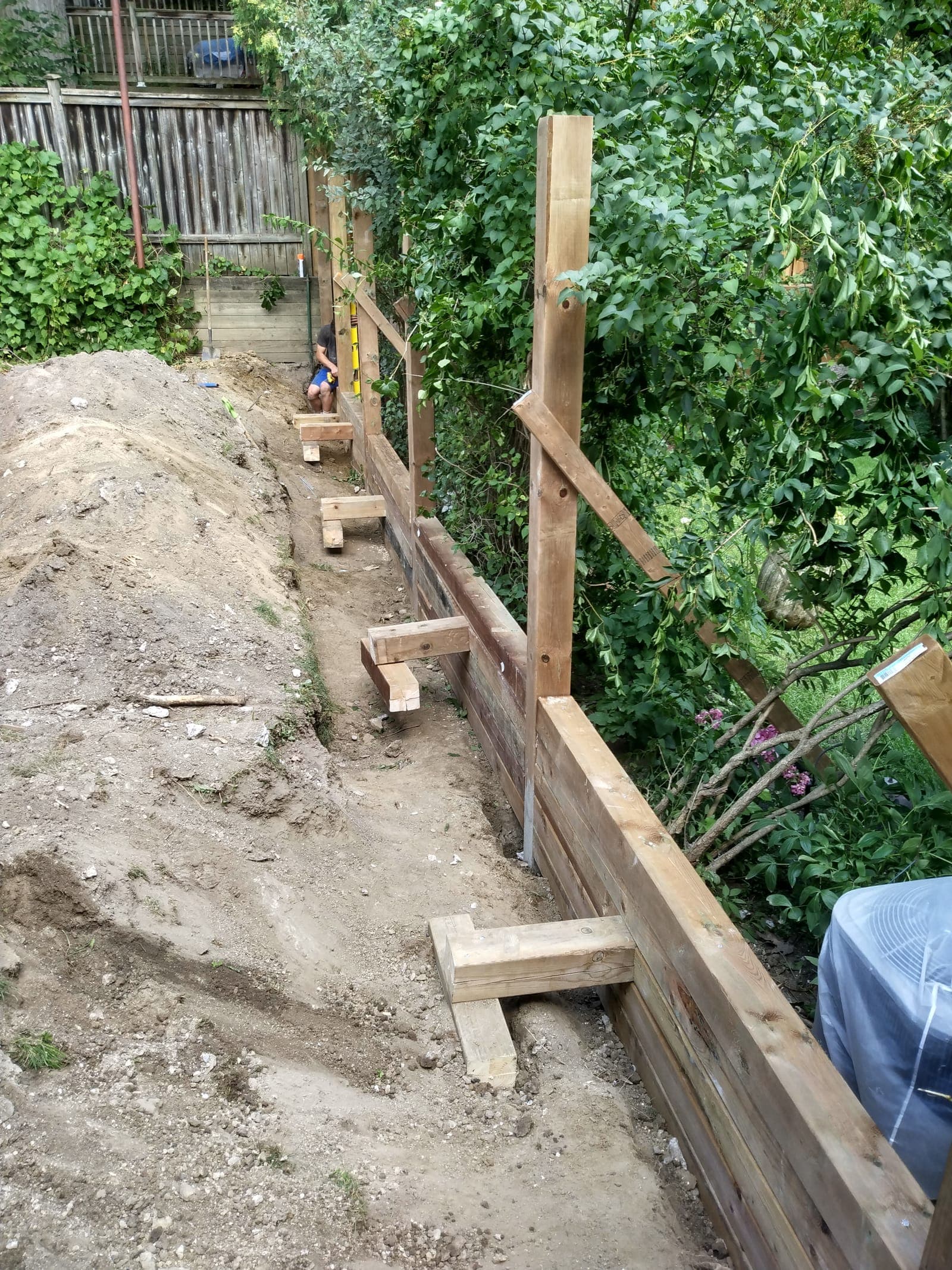 Stacked timber retaining wall with deadman tie-backs holding back a backyard slope