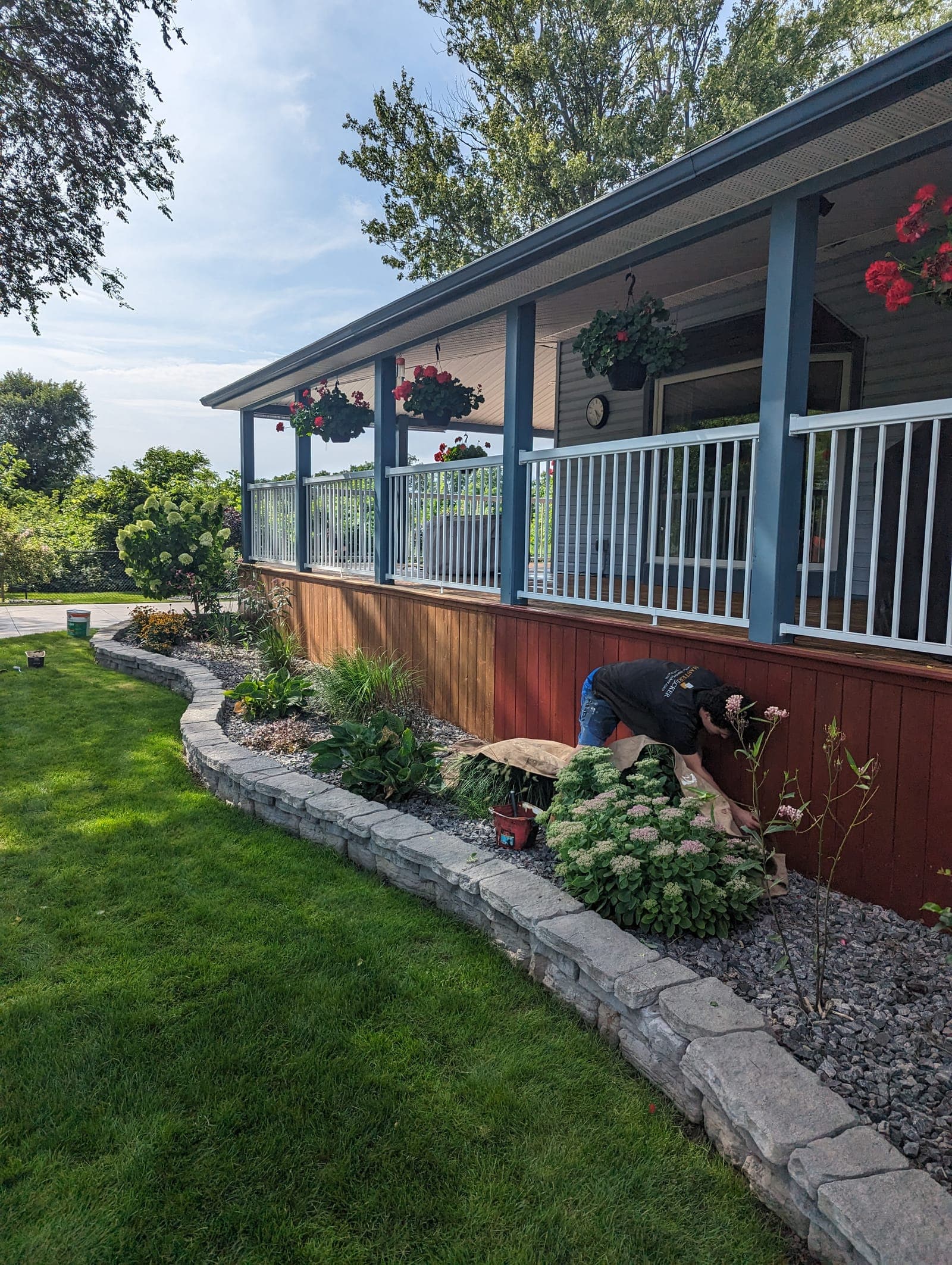 Sweeping stacked-block garden retaining wall bordering a manicured lawn and raised flower bed at a farmhouse porch
