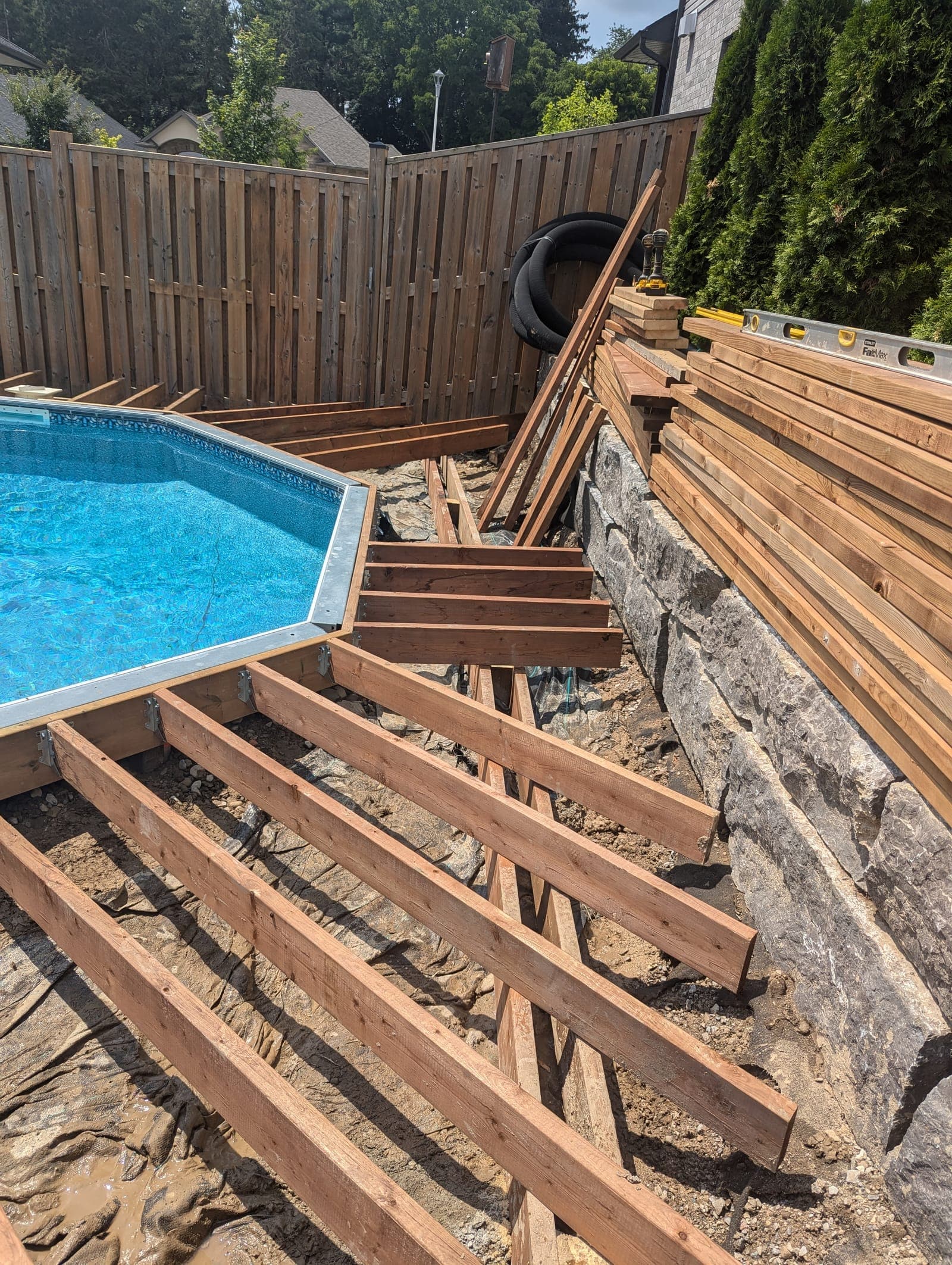 Tall natural stone retaining wall alongside a poolside deck build in a backyard