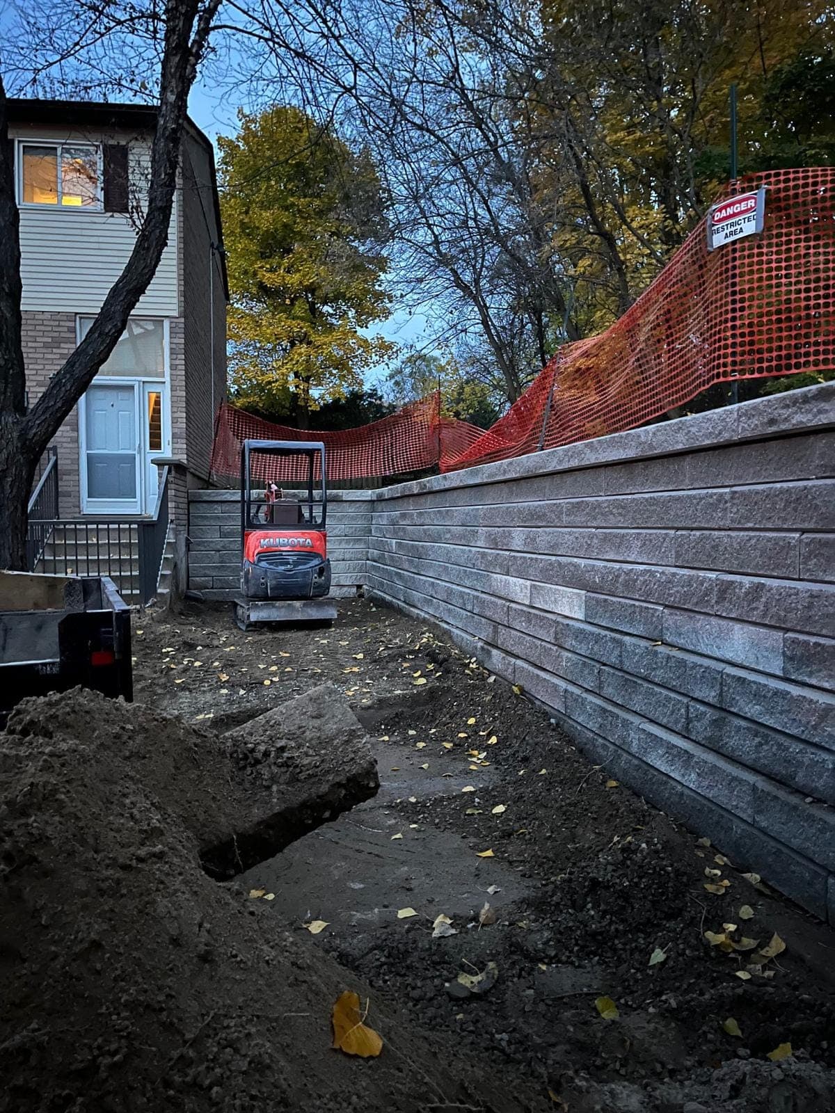 Tall grey segmental block retaining wall curving beside a home during construction