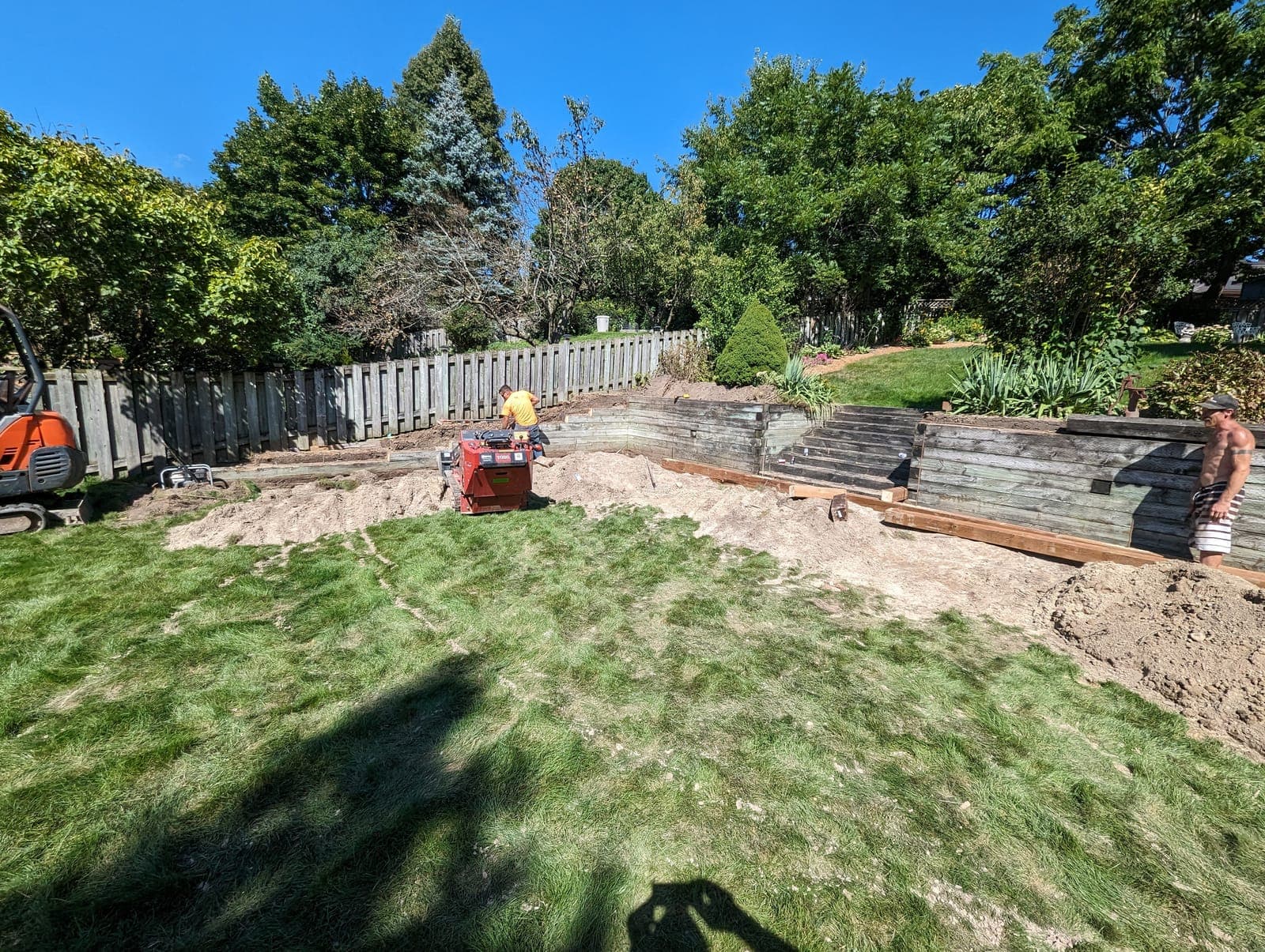 Terraced timber retaining wall spanning a sloped backyard undergoing a landscape renovation