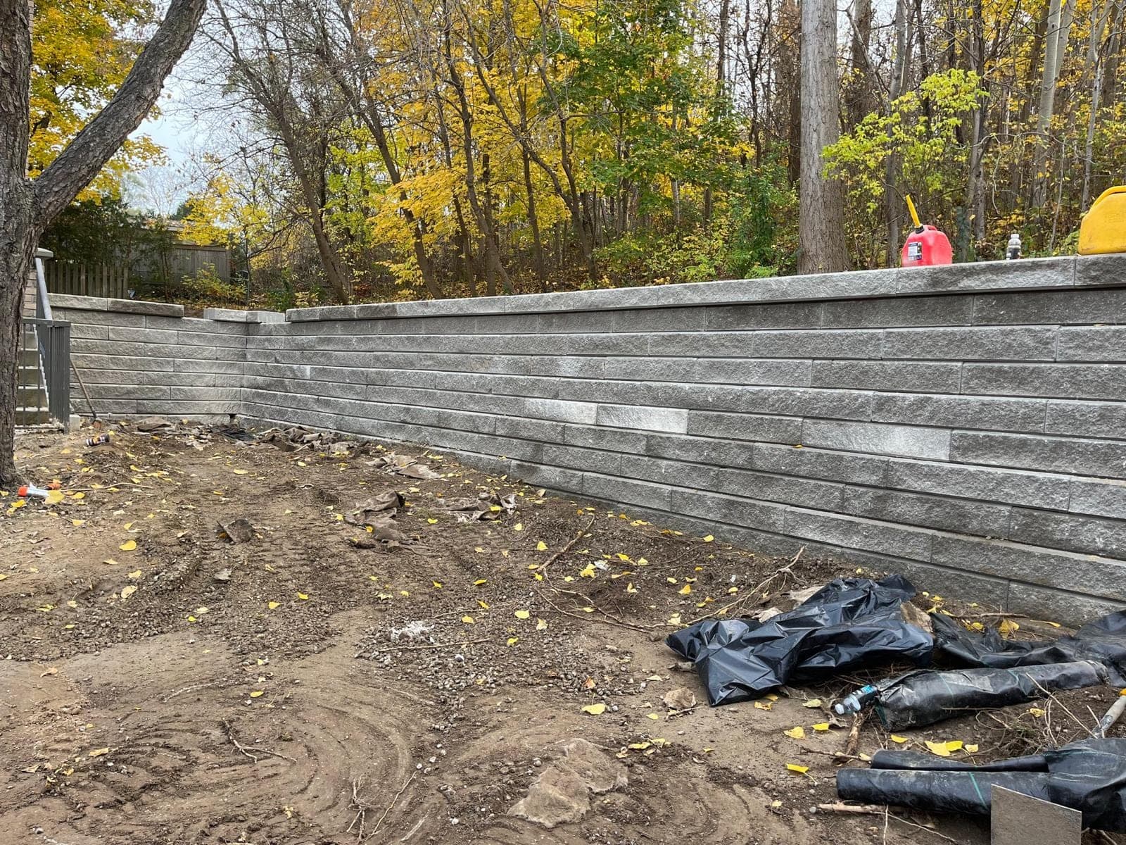 Tiered grey segmental block retaining wall bordering a wooded backyard in autumn