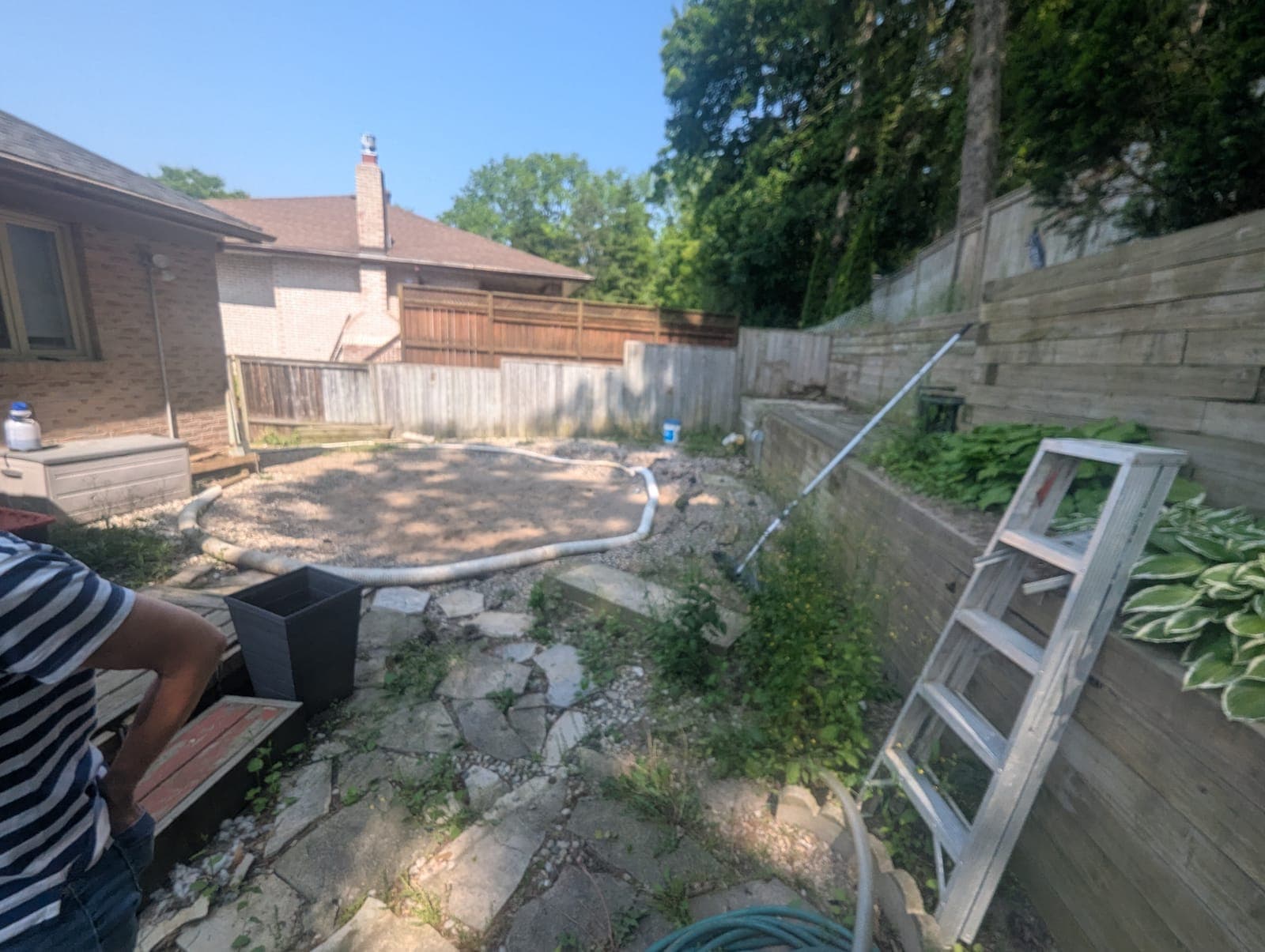 Weathered tiered timber retaining wall holding back a raised garden bed of hostas in a backyard