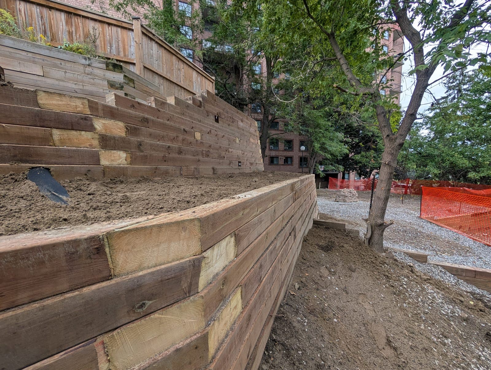 Tiered timber retaining wall stepping back to hold soil beside a fenced urban backyard
