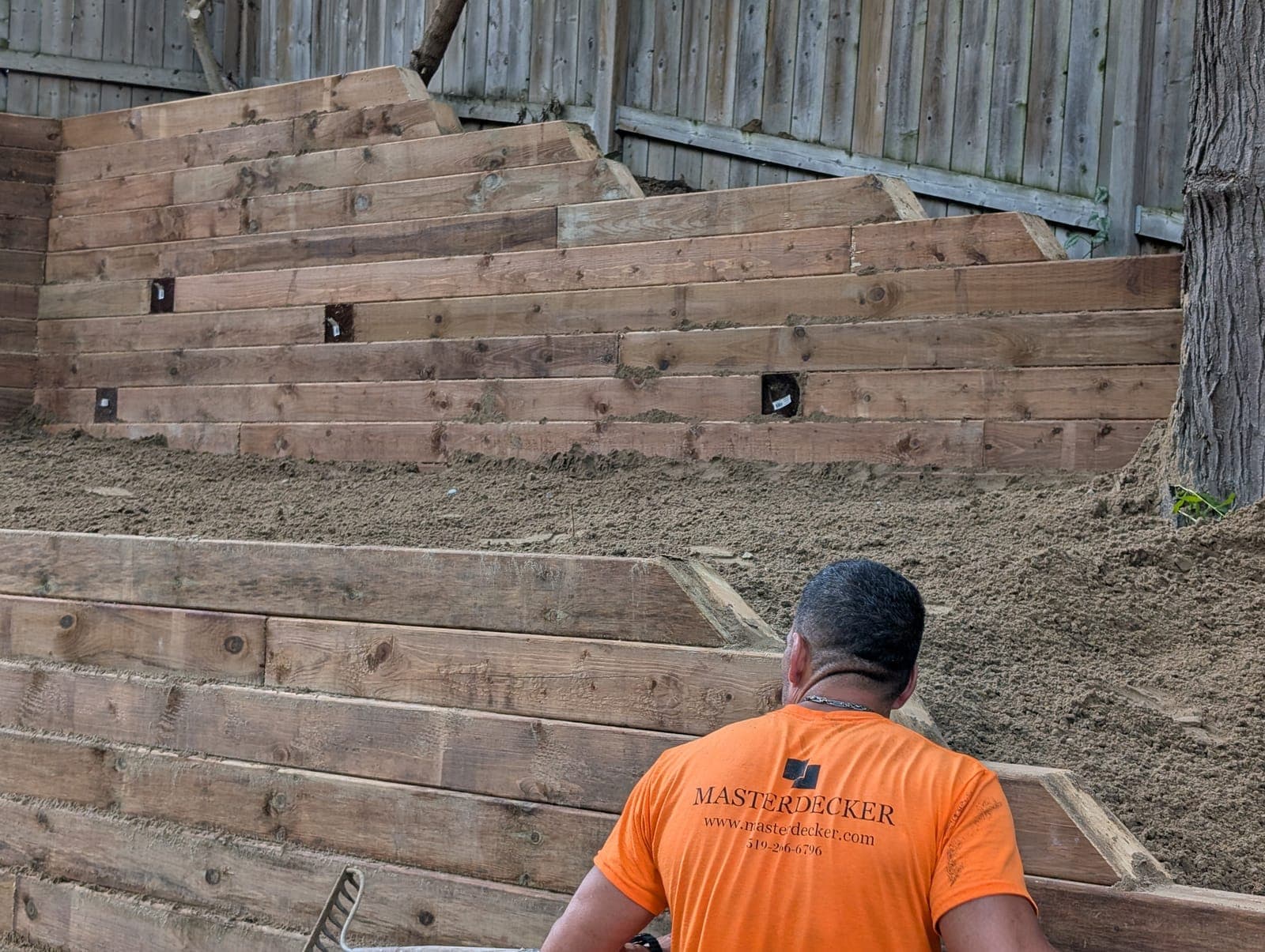 Tiered timber retaining wall with integrated lighting niches during installation in an urban backyard