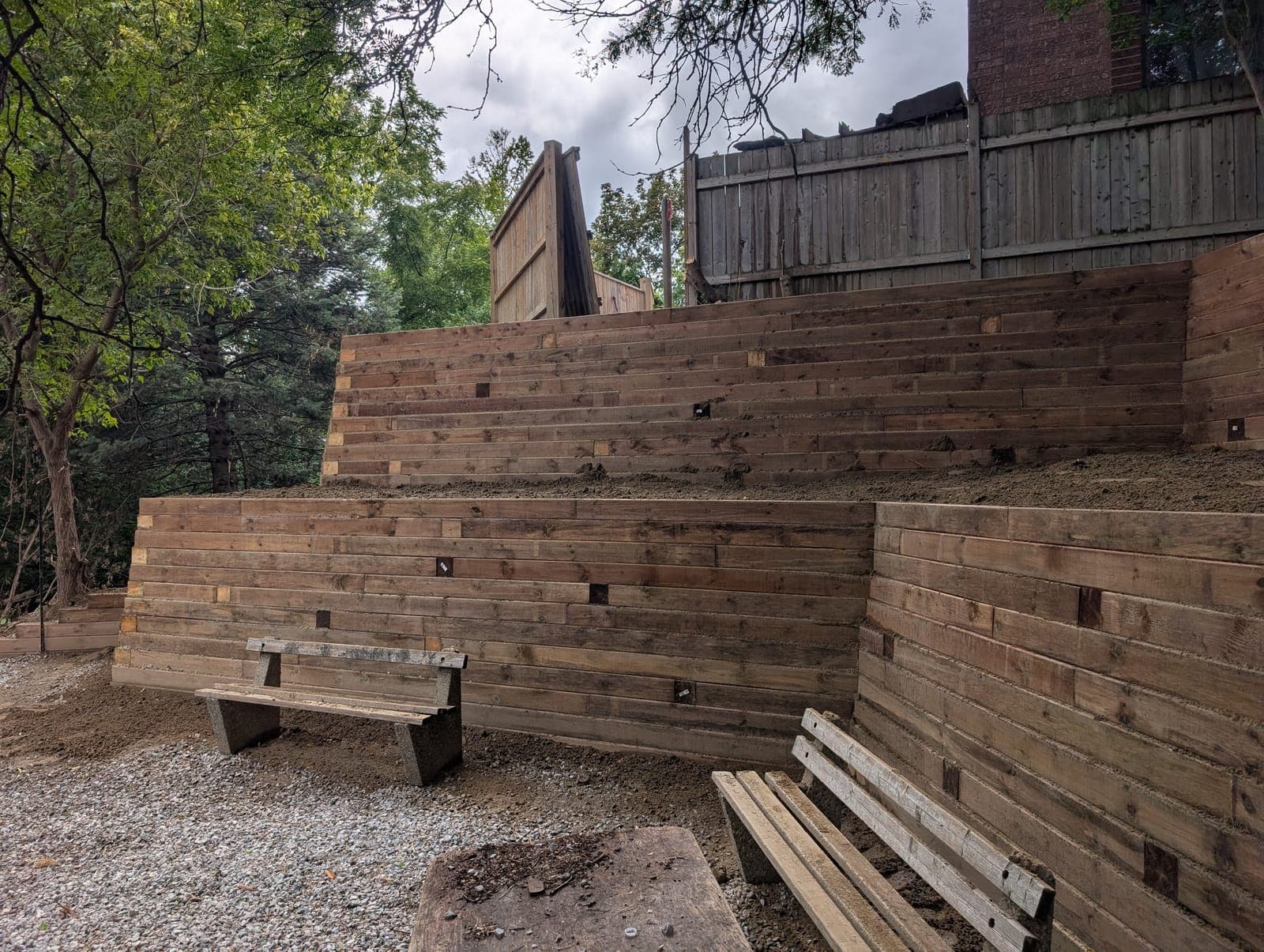 Tiered horizontal timber retaining wall holding back soil in a wooded backyard