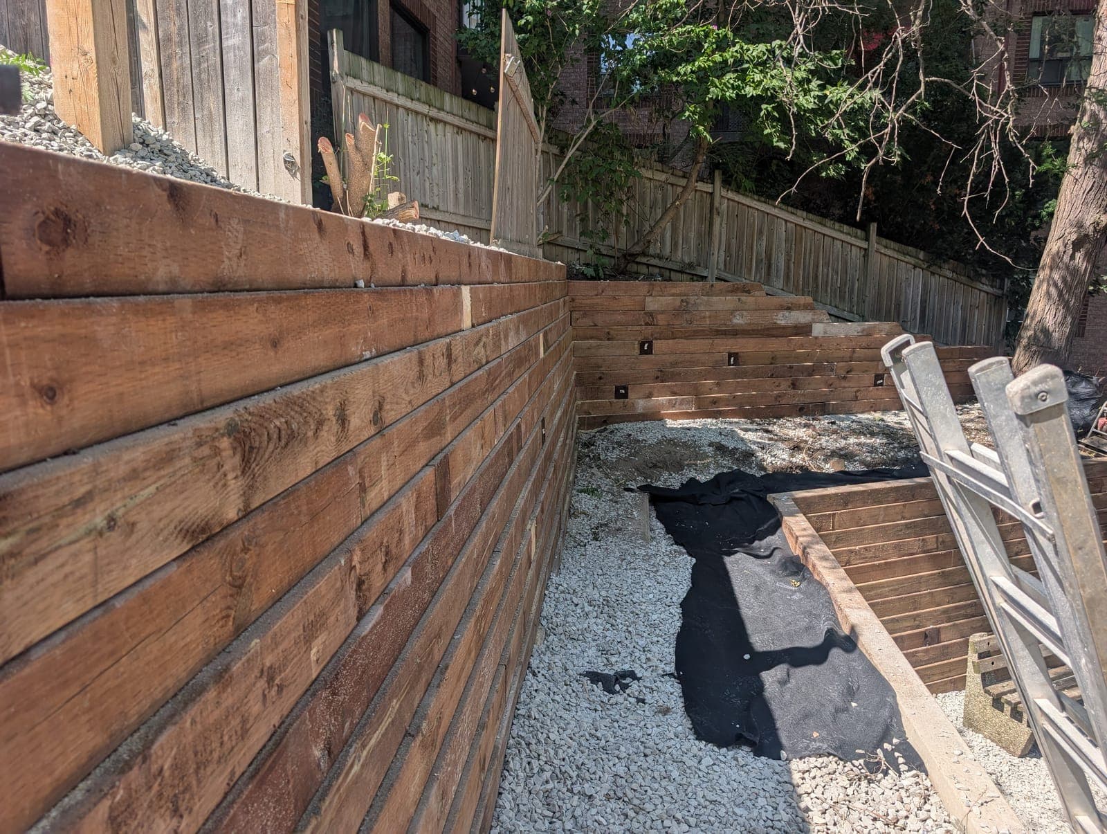 Timber retaining wall running along a gravel walkway with tiered timber walls behind in a backyard