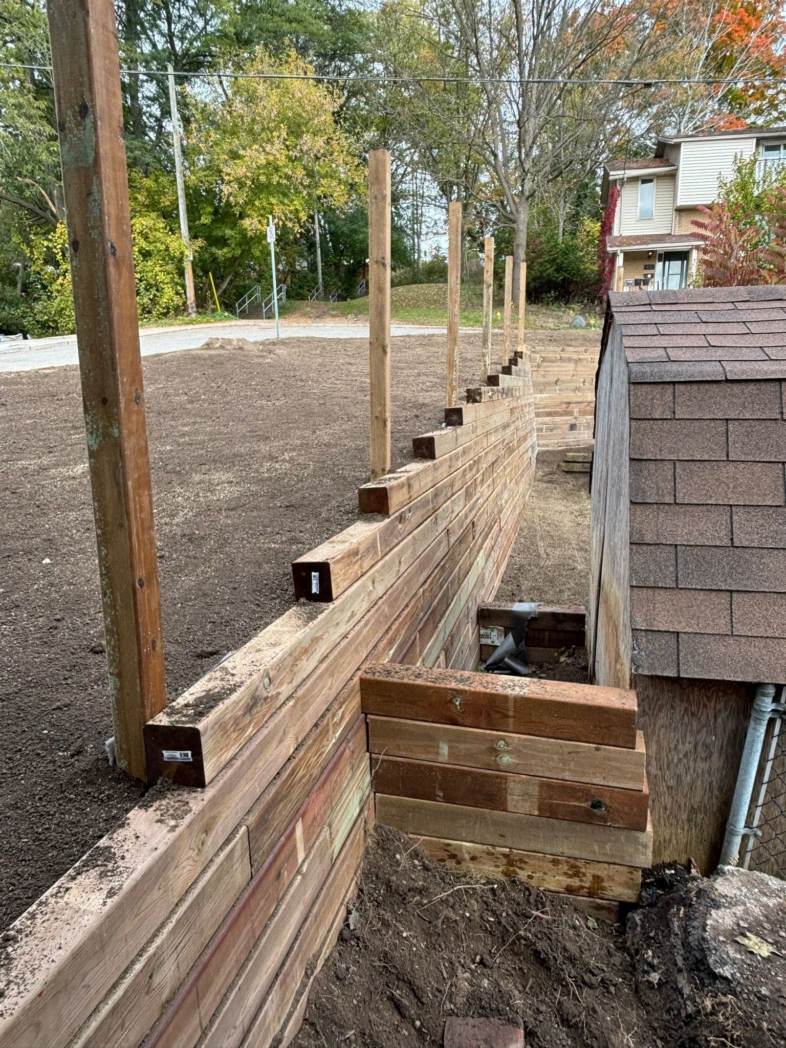 Timber retaining wall under construction with staggered support posts holding back backyard soil