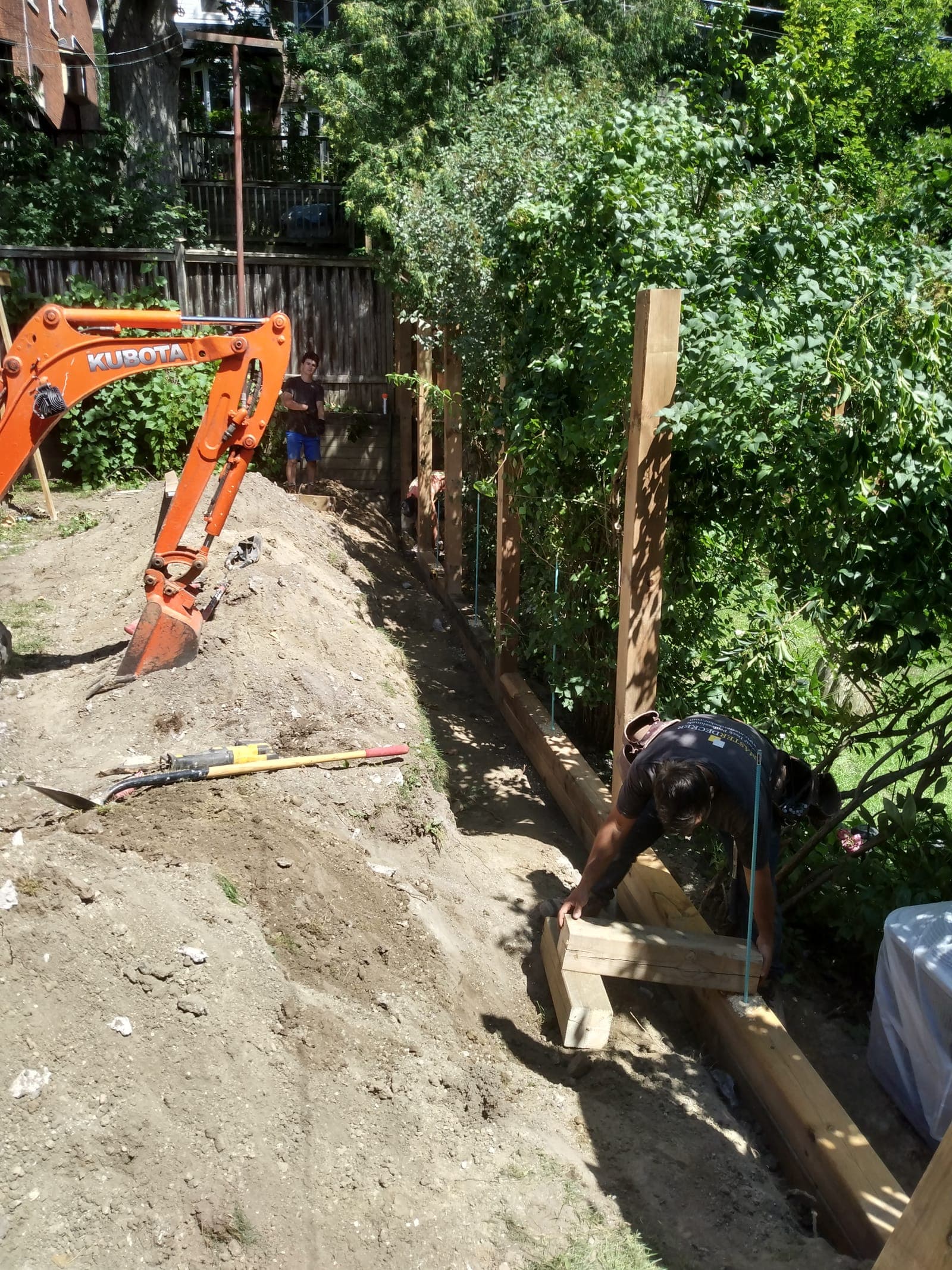Pressure-treated timber retaining wall under construction with vertical support posts along a backyard slope