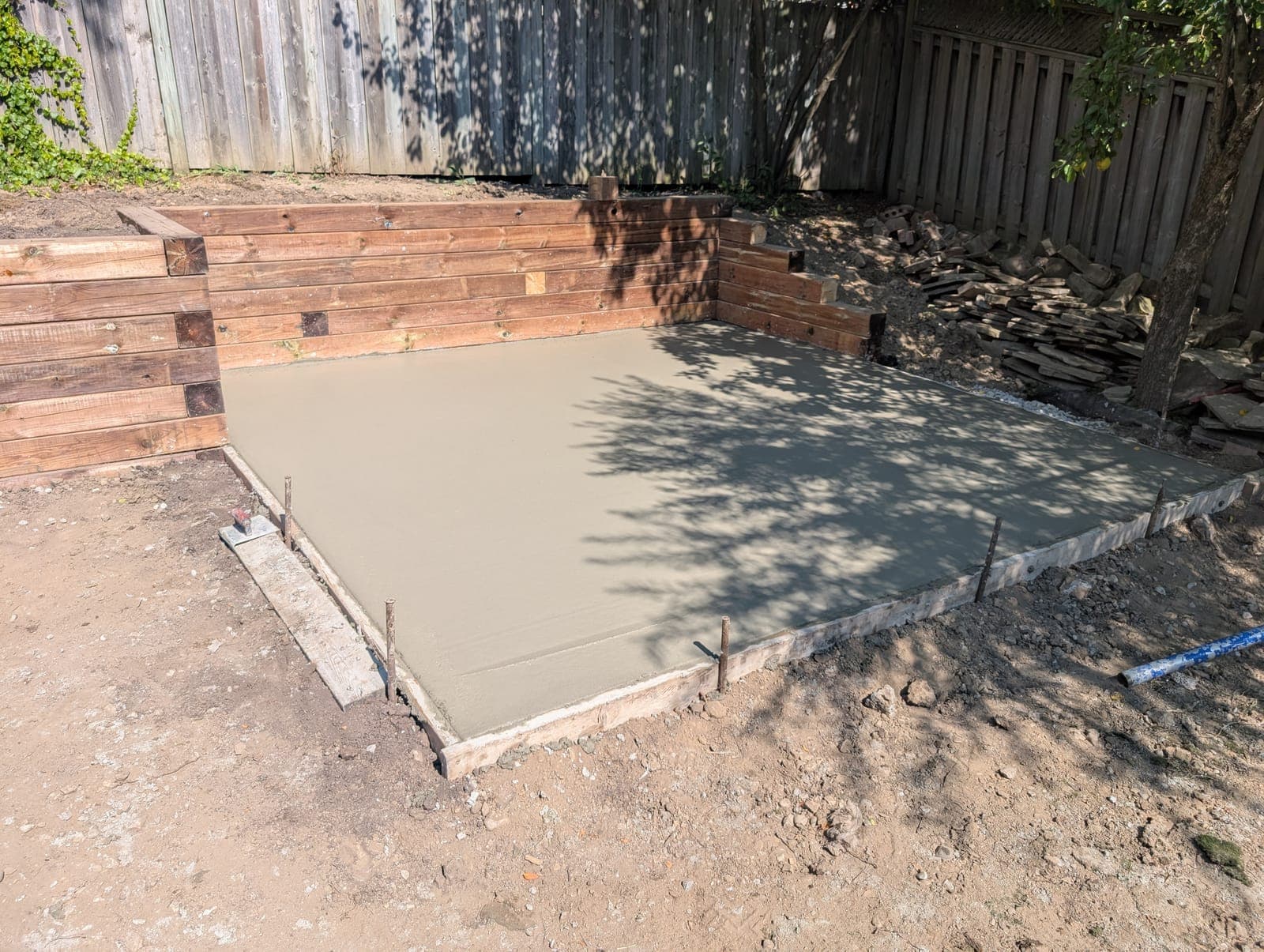 L-shaped timber retaining wall surrounding a freshly poured concrete pad in a backyard