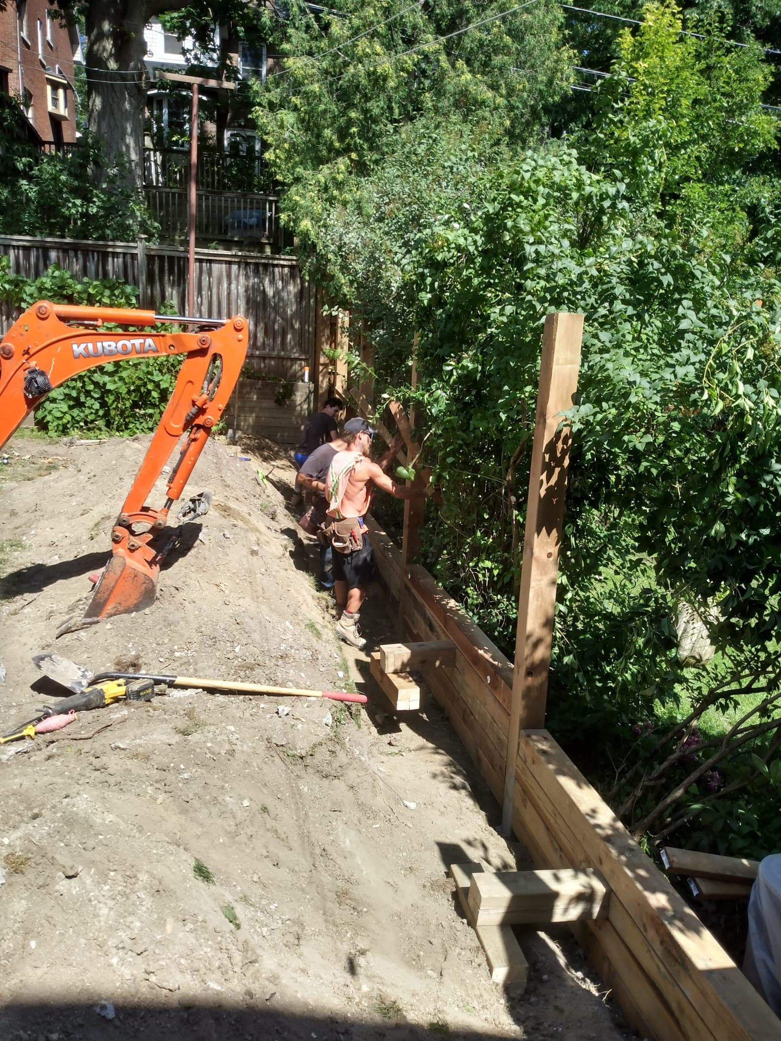 Landscaping crew building a stacked timber retaining wall along a residential backyard slope