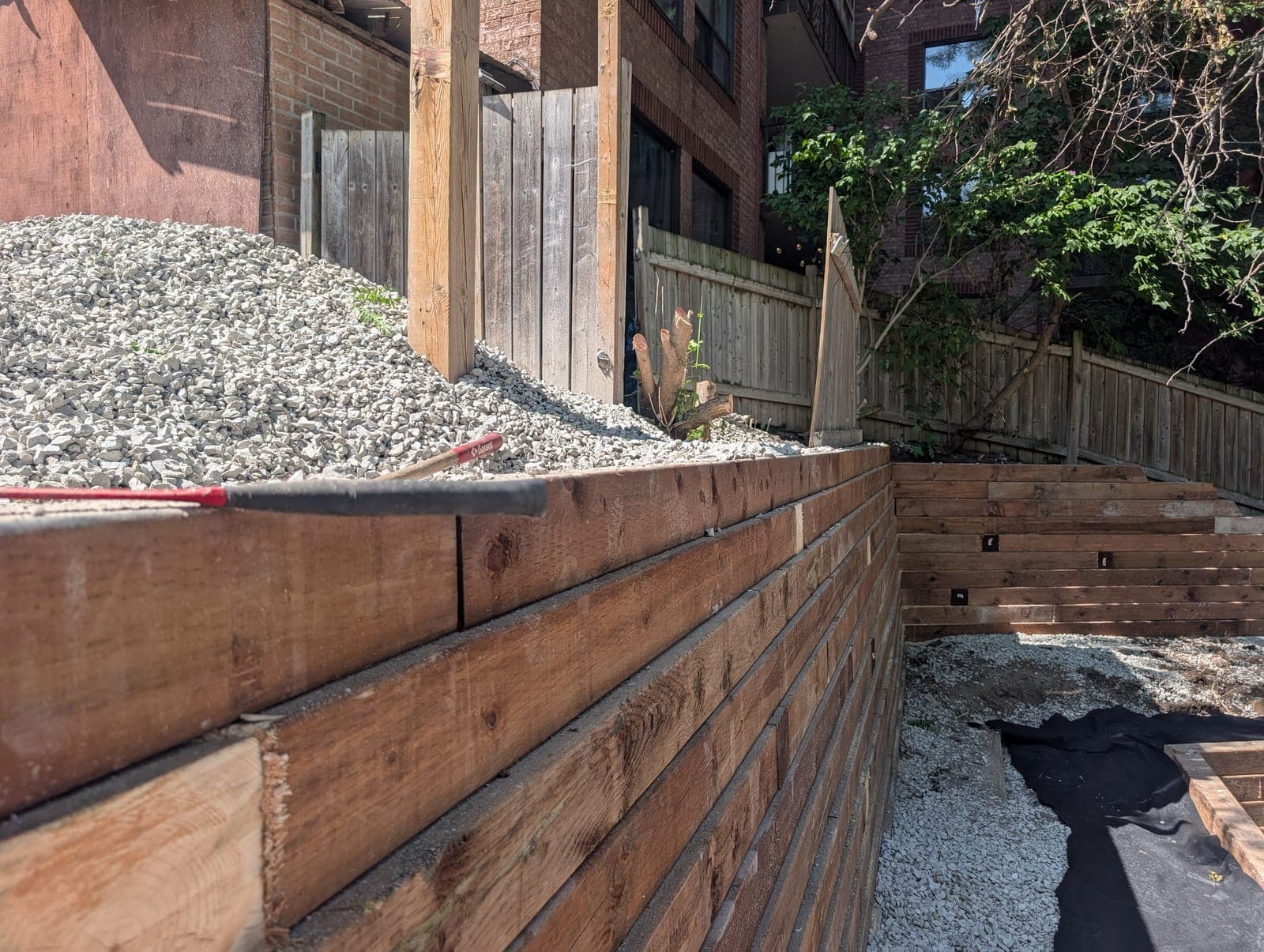 Close view of a timber retaining wall retaining gravel backfill on a landscaped backyard slope
