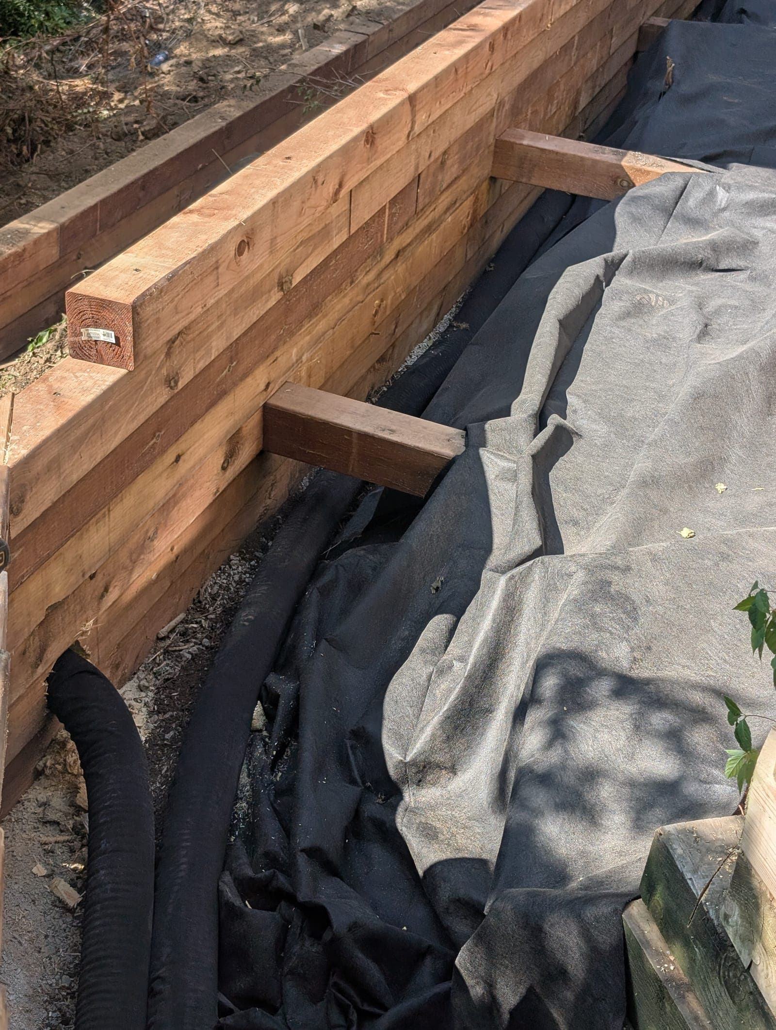 Close-up of a timber retaining wall showing a deadman anchor and perforated drain pipe with filter fabric