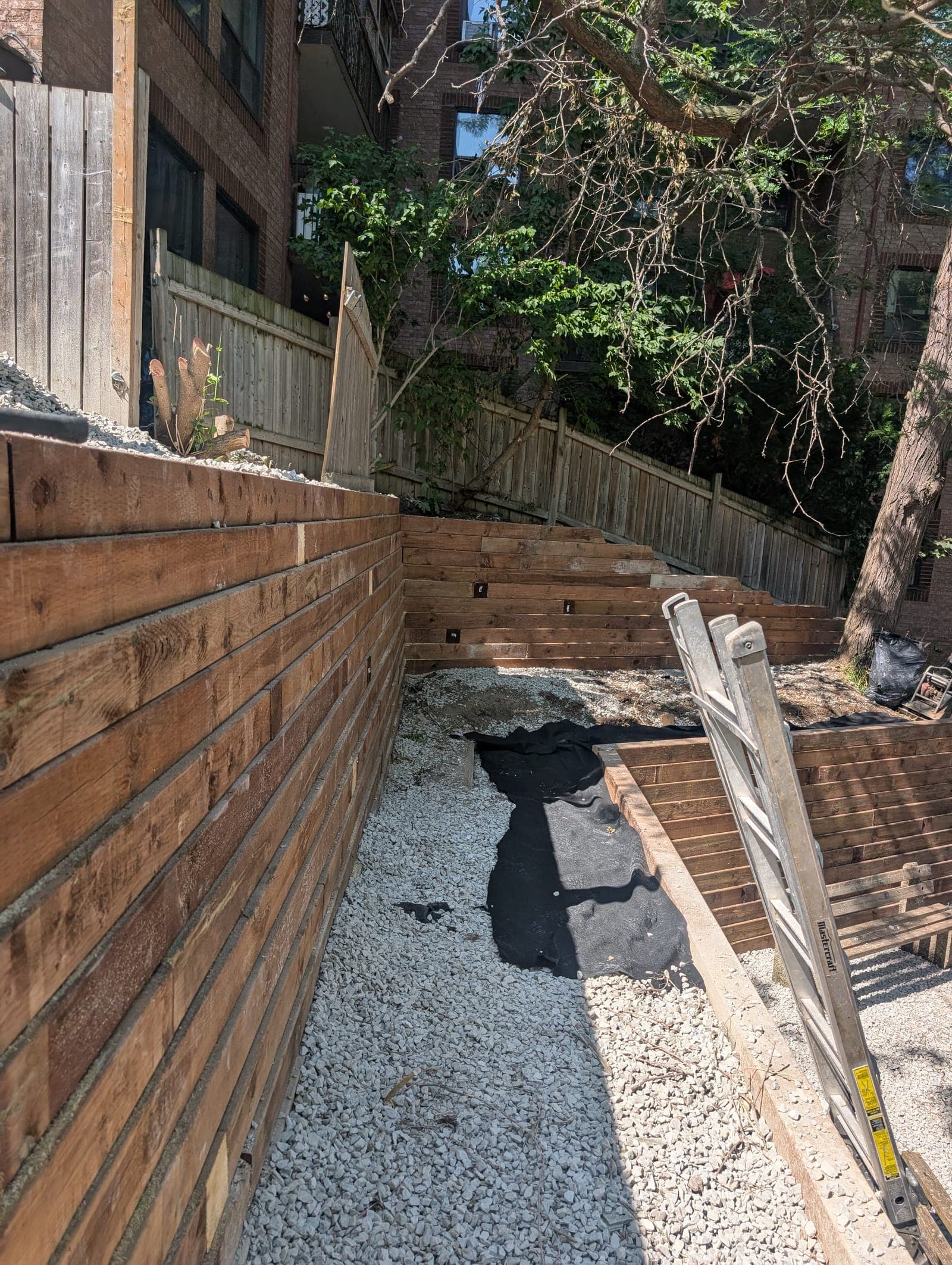 Timber retaining wall holding back gravel backfill beside tiered timber walls in an urban backyard