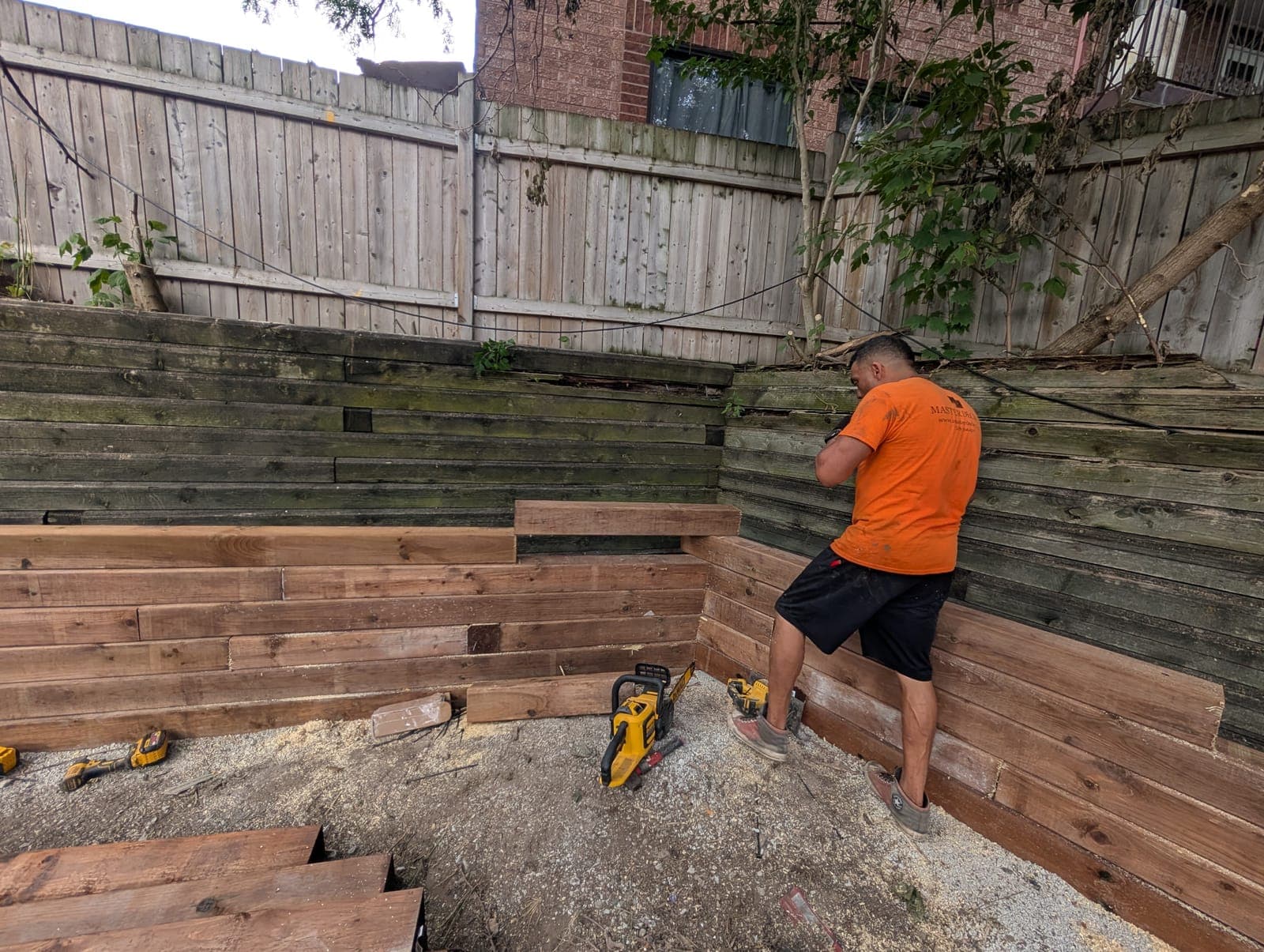Contractor installing a stacked timber tie retaining wall against a backyard slope