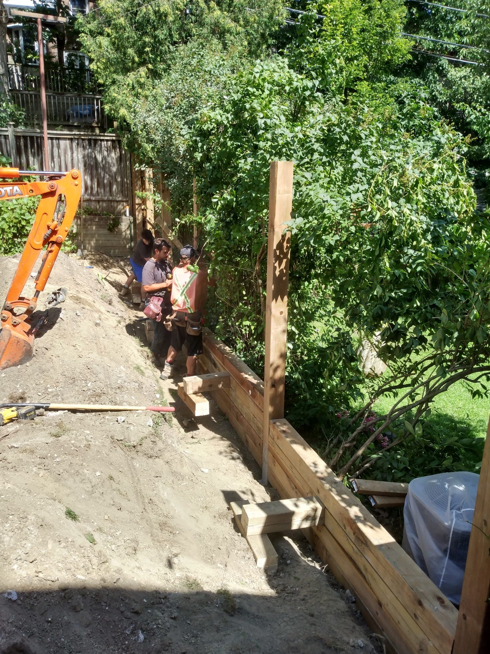 Crew installing a pressure-treated timber retaining wall along a backyard grade change