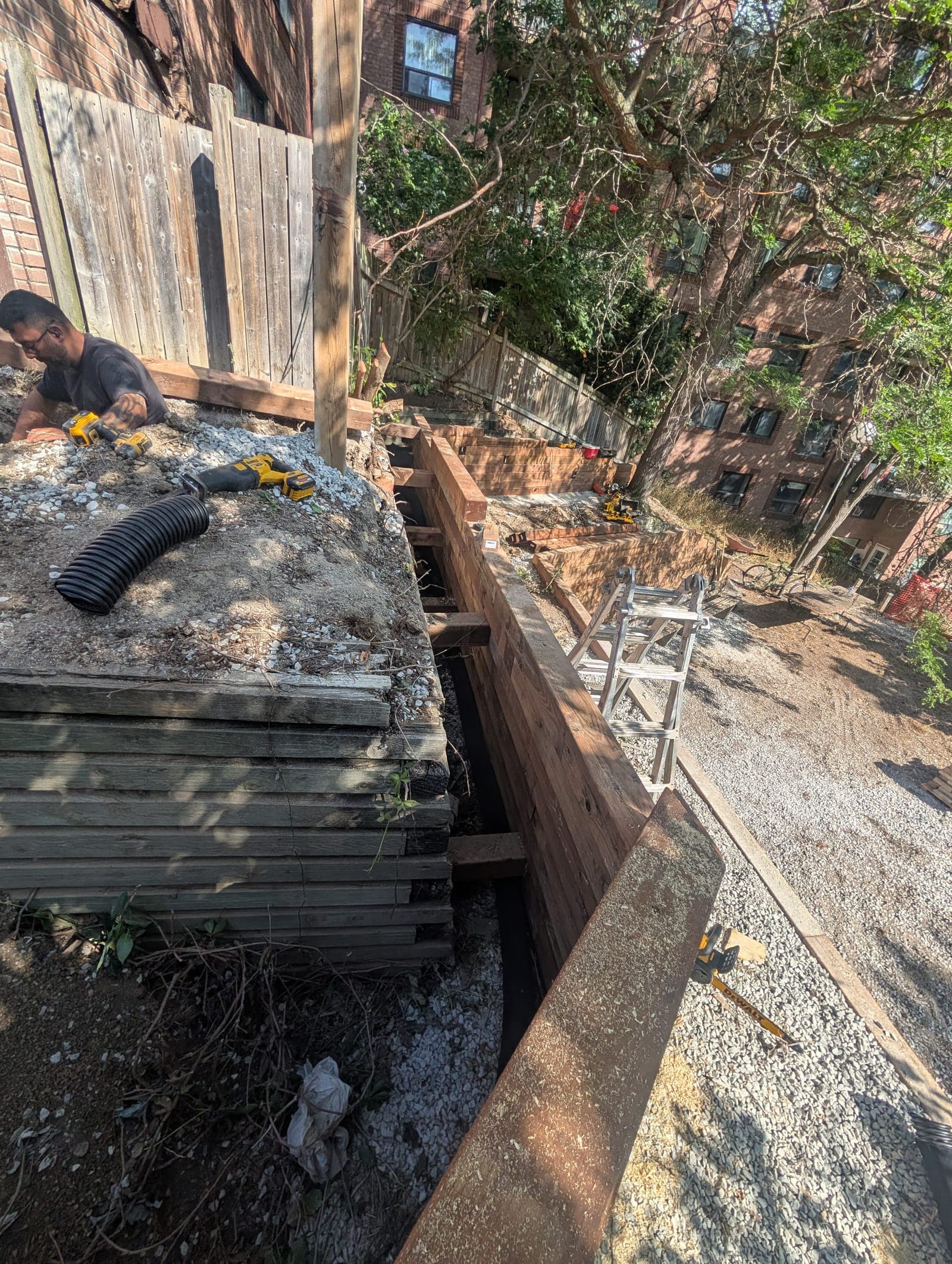 Timber retaining wall installation in progress alongside a gravel access lane in an urban backyard